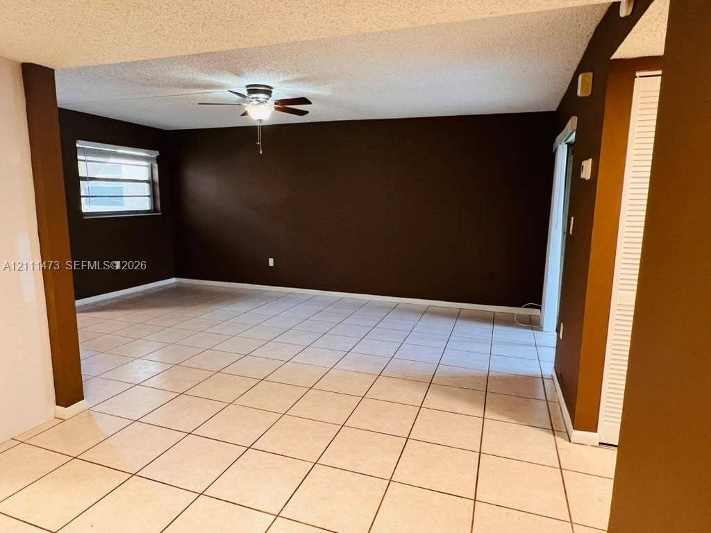 11101 Royal Palm Boulevard, #113, Coral Springs, Coral Springs, FL 33065 Open-concept interior featuring light-toned tile flooring, a ceiling fan with integrated light fixture, recessed window with horizontal blinds, and louvered closet doors