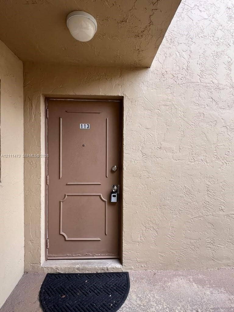 11101 Royal Palm Boulevard, #113, Coral Springs, Coral Springs, FL 33065 Exterior entrance featuring a solid-core door with decorative panel molding, a flush-mount overhead ceiling light, and textured stucco walls