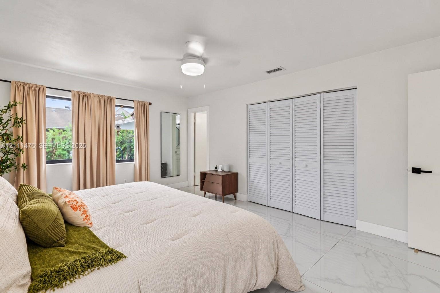 Large-format tile flooring, ceiling fan with integrated lighting, and white louvered-door closet cabinetry