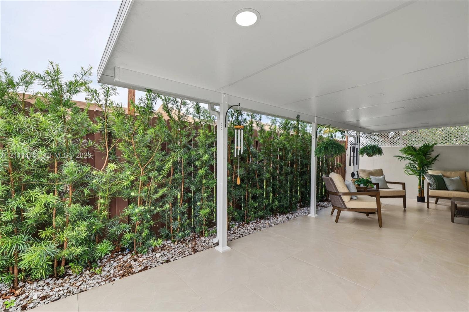 Covered patio featuring large-format tile flooring, recessed lighting, and a perimeter of mature landscaping set against a privacy fence