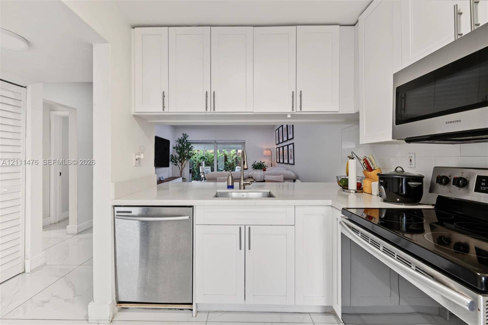 Kitchen featuring white shaker-style cabinetry, stainless steel appliances, neutral stone-finish countertops, an undermount sink, and large-format tile flooring
