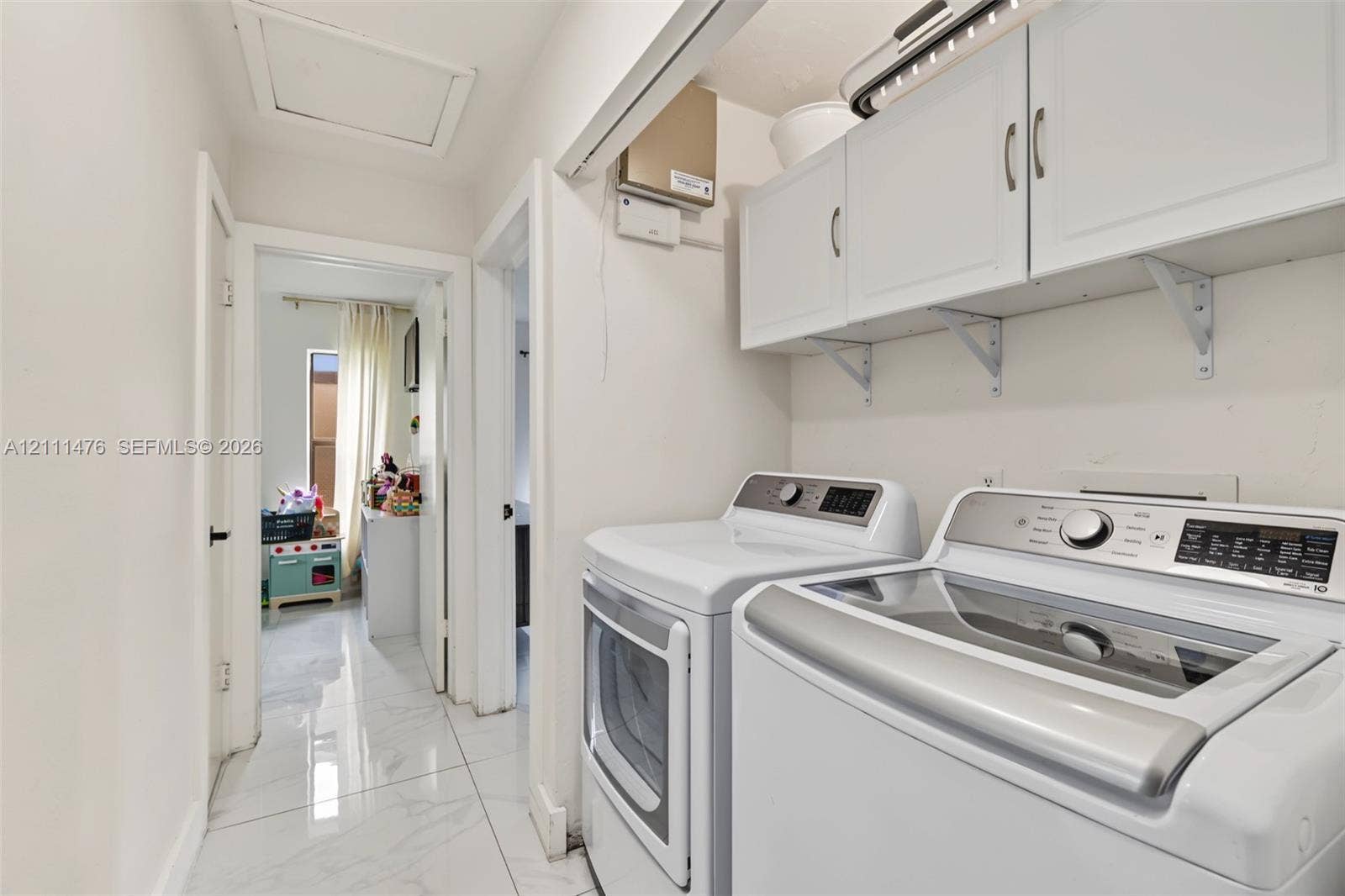 Laundry area featuring white shaker-style wall-mounted cabinetry, polished stone-finish flooring, and recessed ceiling lighting