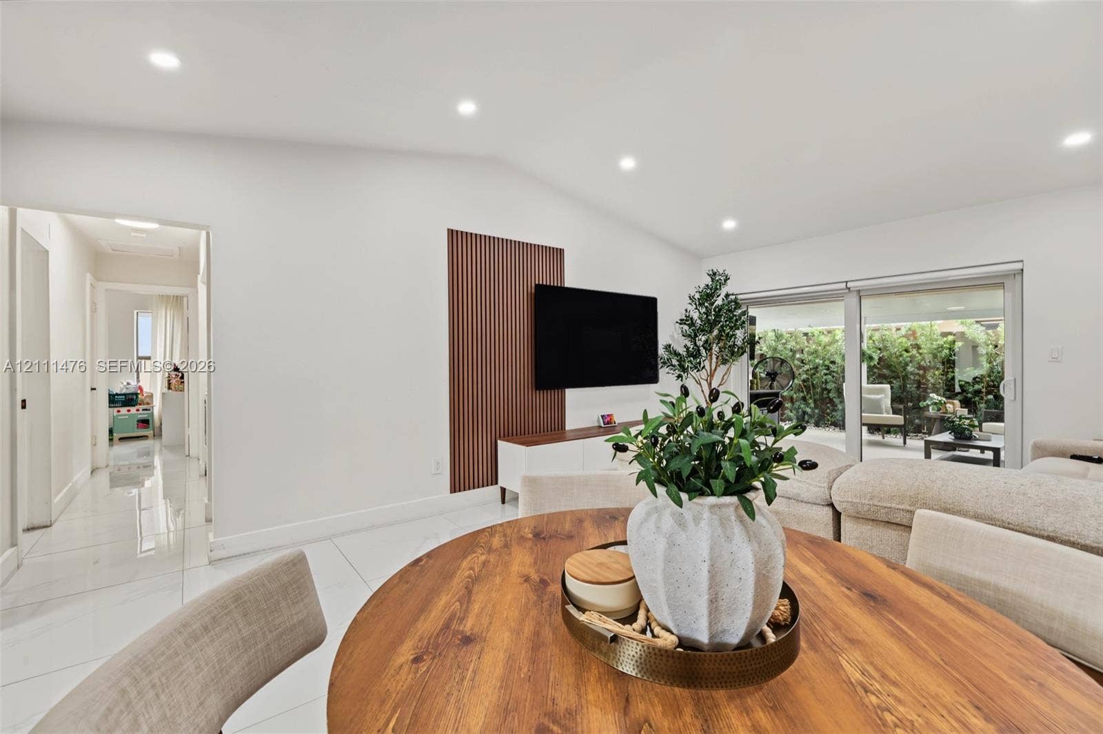 Open-concept room featuring high ceilings with recessed lighting, large-format tile flooring, a floor-to-ceiling wood slat accent wall, and sliding glass doors