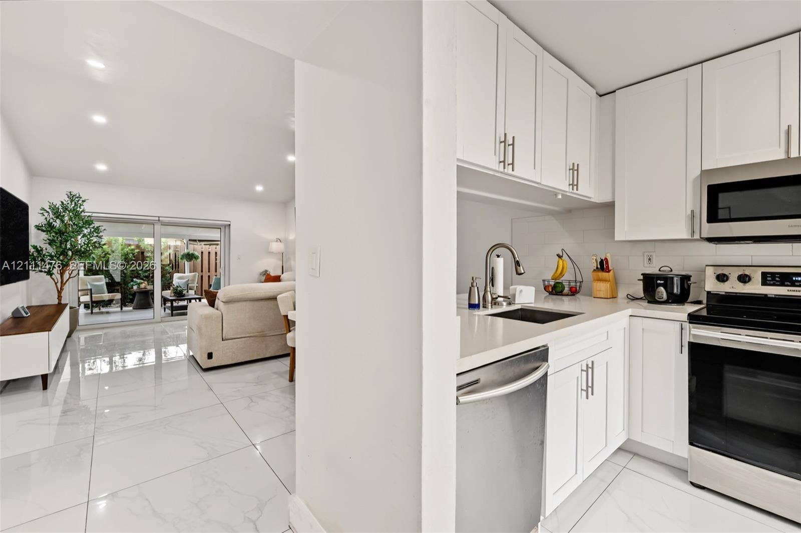 Kitchen featuring white cabinetry, solid-surface countertops, subway tile backsplash, and stainless steel appliances, complemented by polished tile flooring throughout