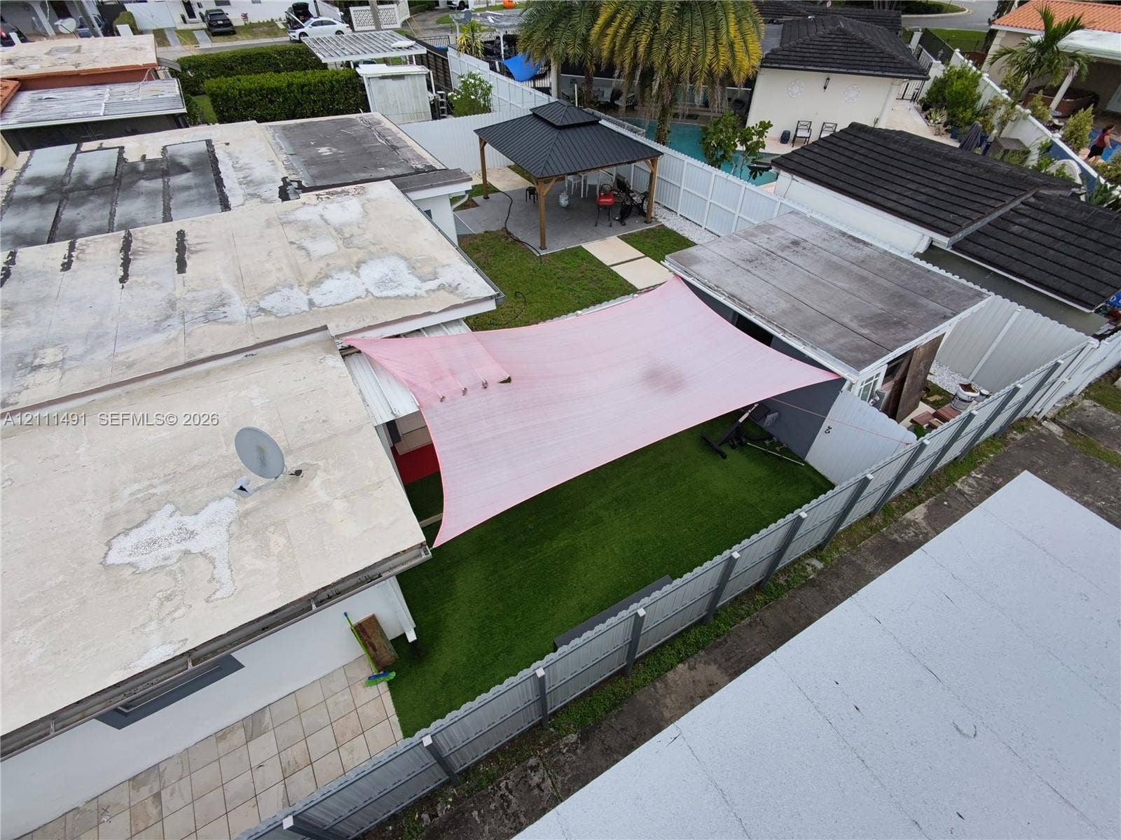 Fenced backyard featuring synthetic turf, a detached pavilion, paver patio, and a fixed overhead shade canopy