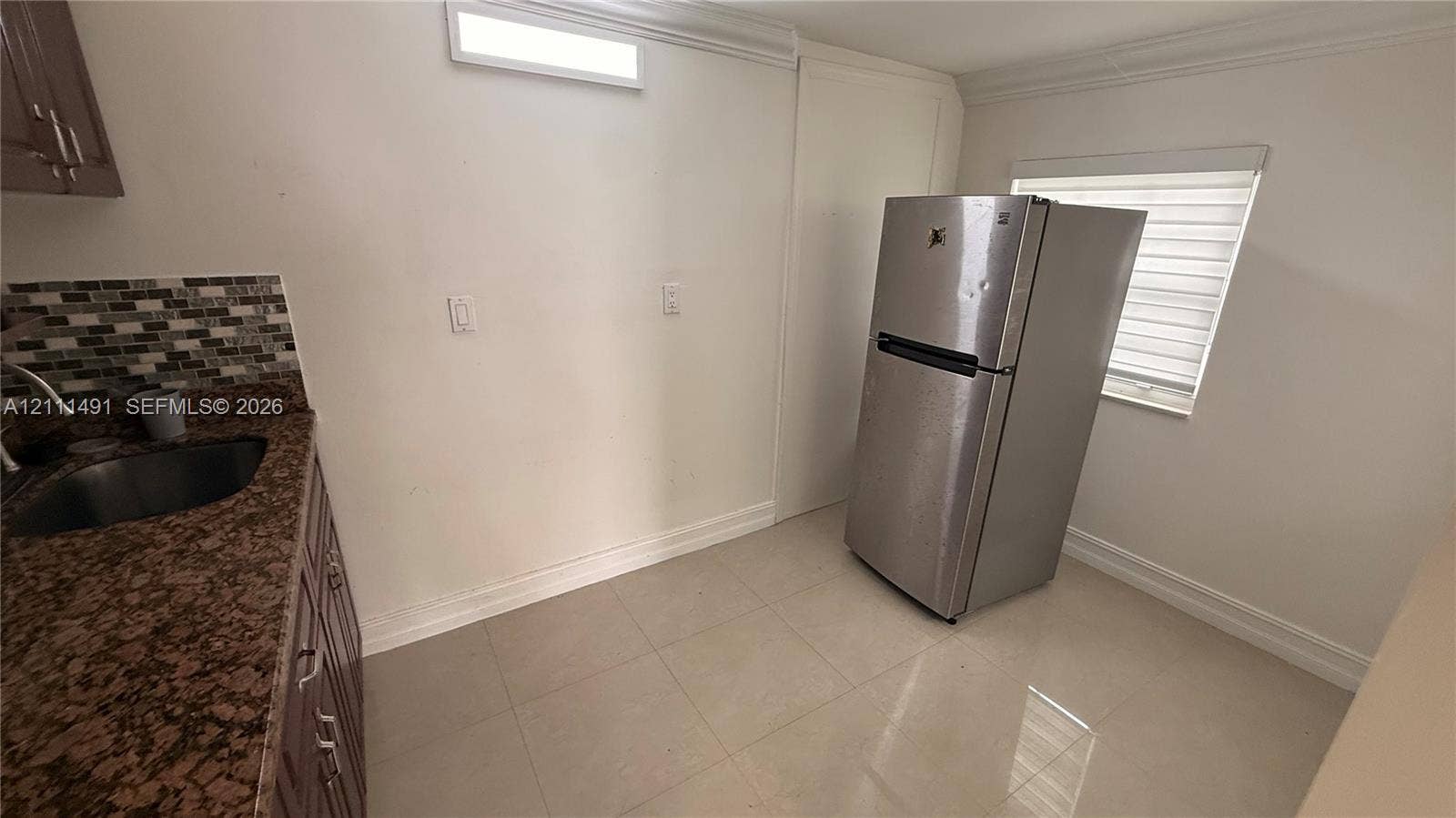 Stone-surfaced countertop, stainless steel sink, multi-tonal mosaic tile backsplash, built-in cabinetry, and tile flooring