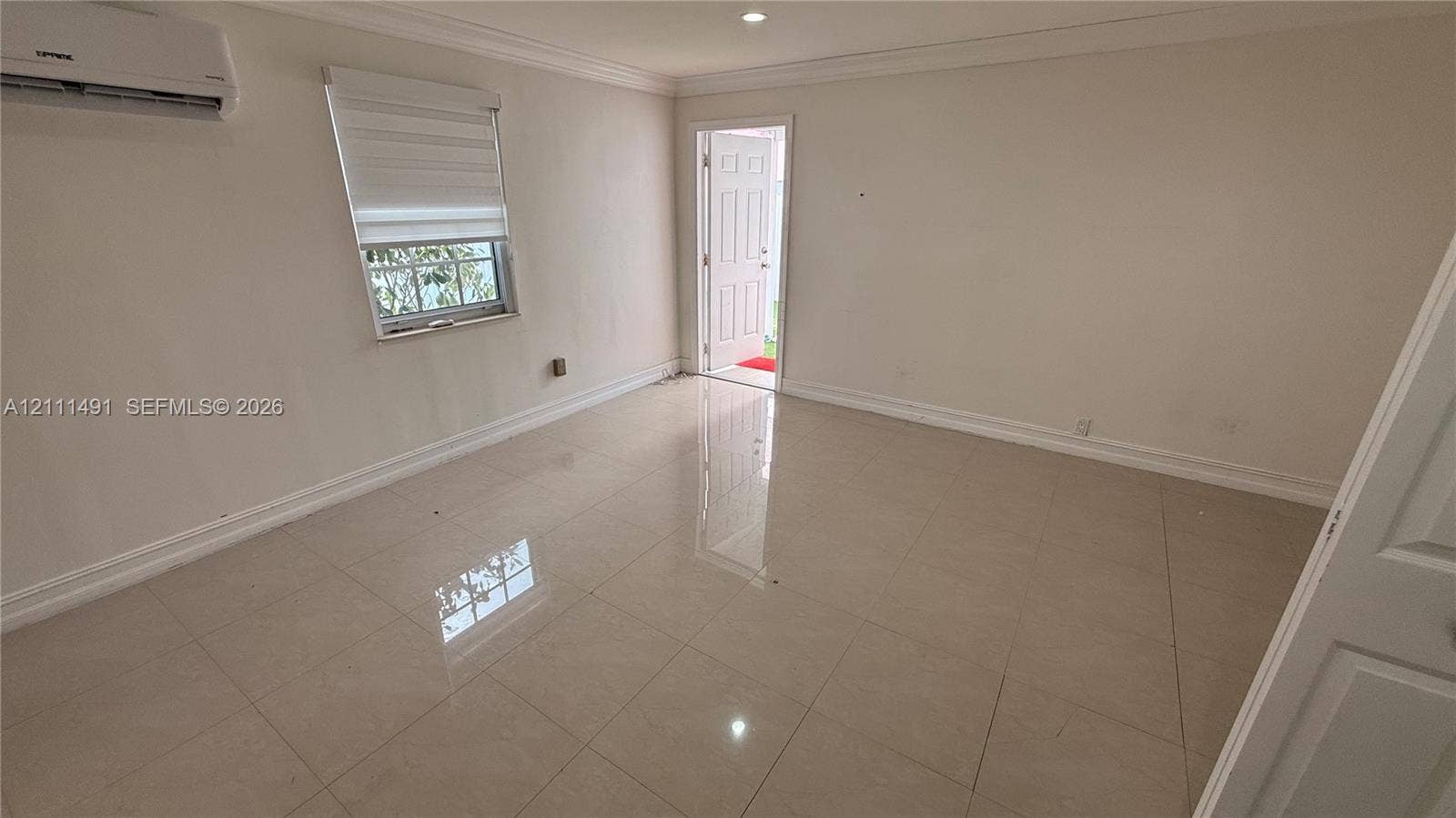 Neutral-toned interior featuring large-format tile flooring, crown molding, a wall-mounted ductless mini-split system, and recessed lighting
