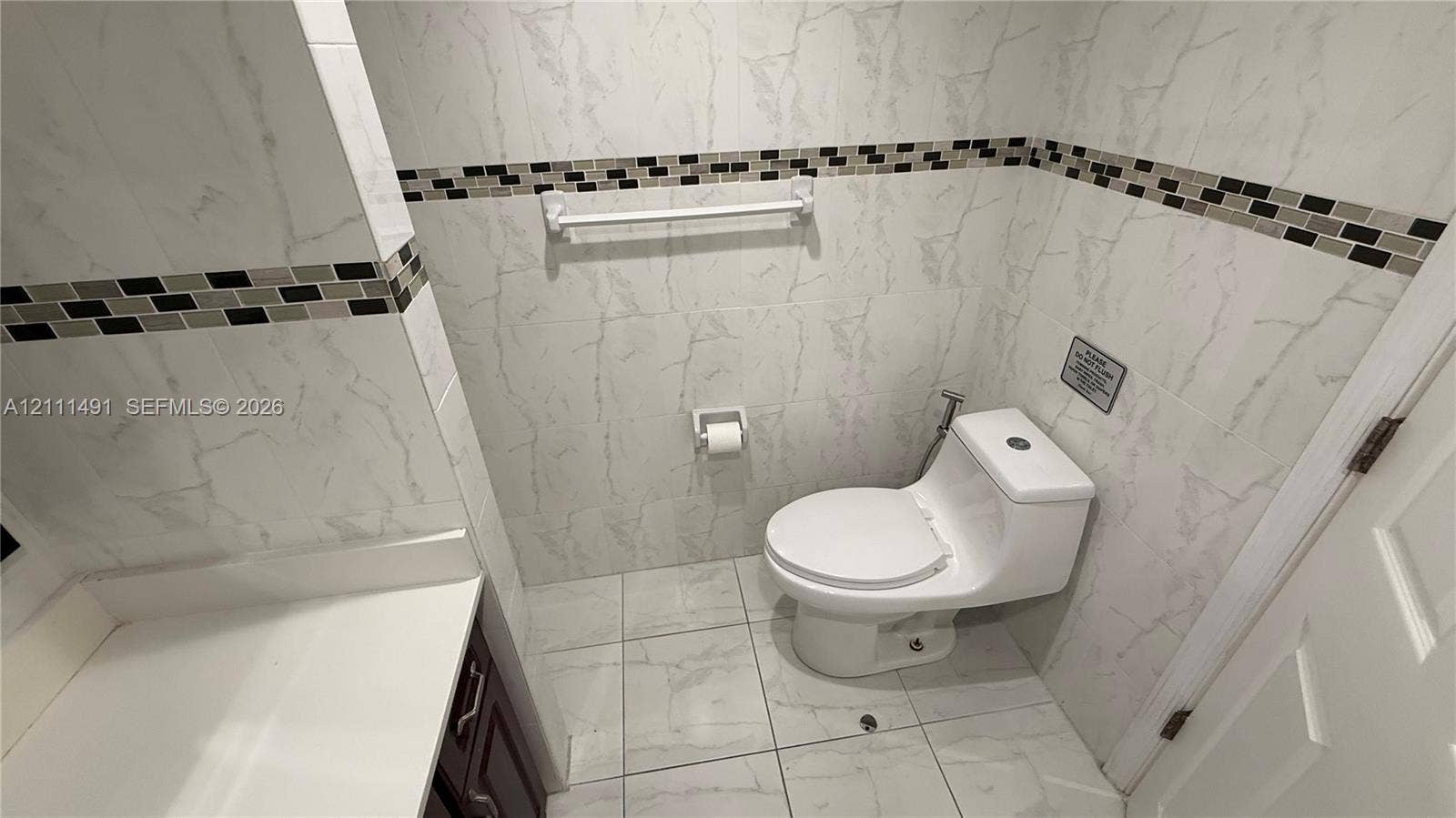 Bathroom featuring full-height wall tiling, integrated mosaic accent banding, large-format porcelain floor tile, and a one-piece toilet