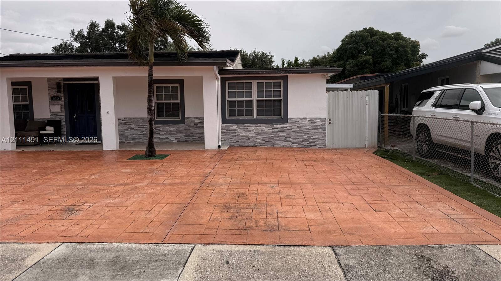 Exterior facade featuring stone veneer detailing, a covered entryway, stamped concrete driveway, and white privacy fencing