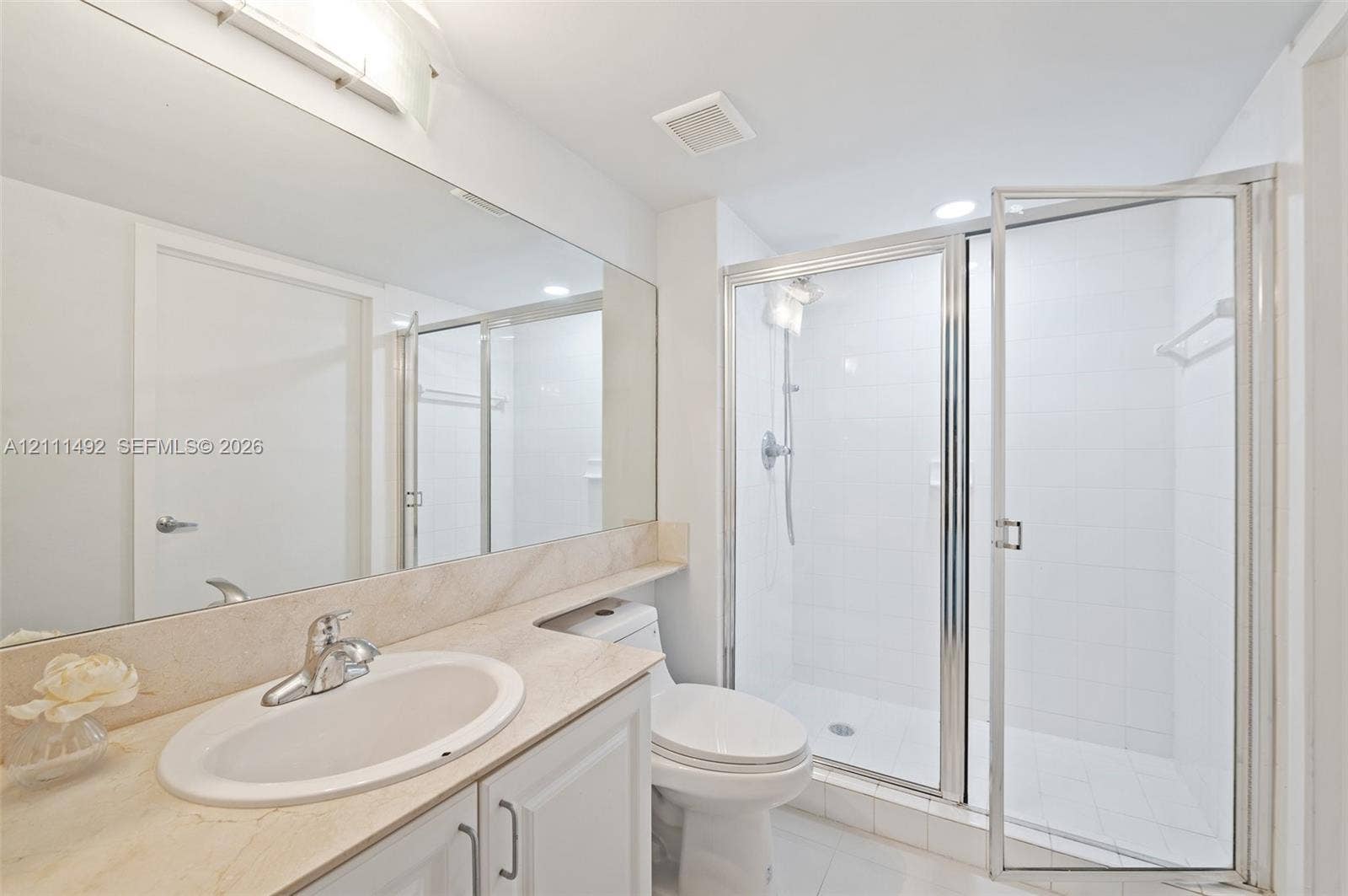 Bathroom featuring an integrated vanity with a stone-finish countertop, full-width vanity mirror, polished chrome faucet, and a walk-in shower with a glass enclosure