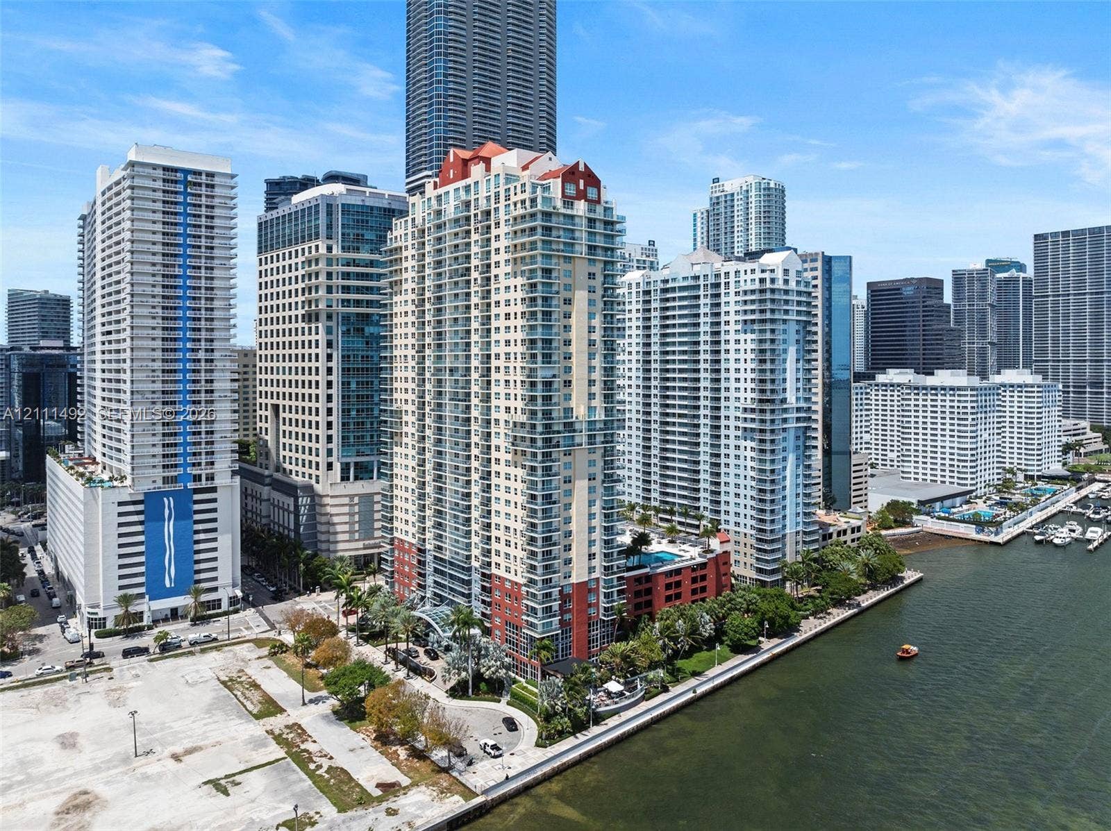 High-rise residential tower featuring a multi-story exterior, stacked glass balconies, a red-tiled roofline, and ground-level porte-cochre entry