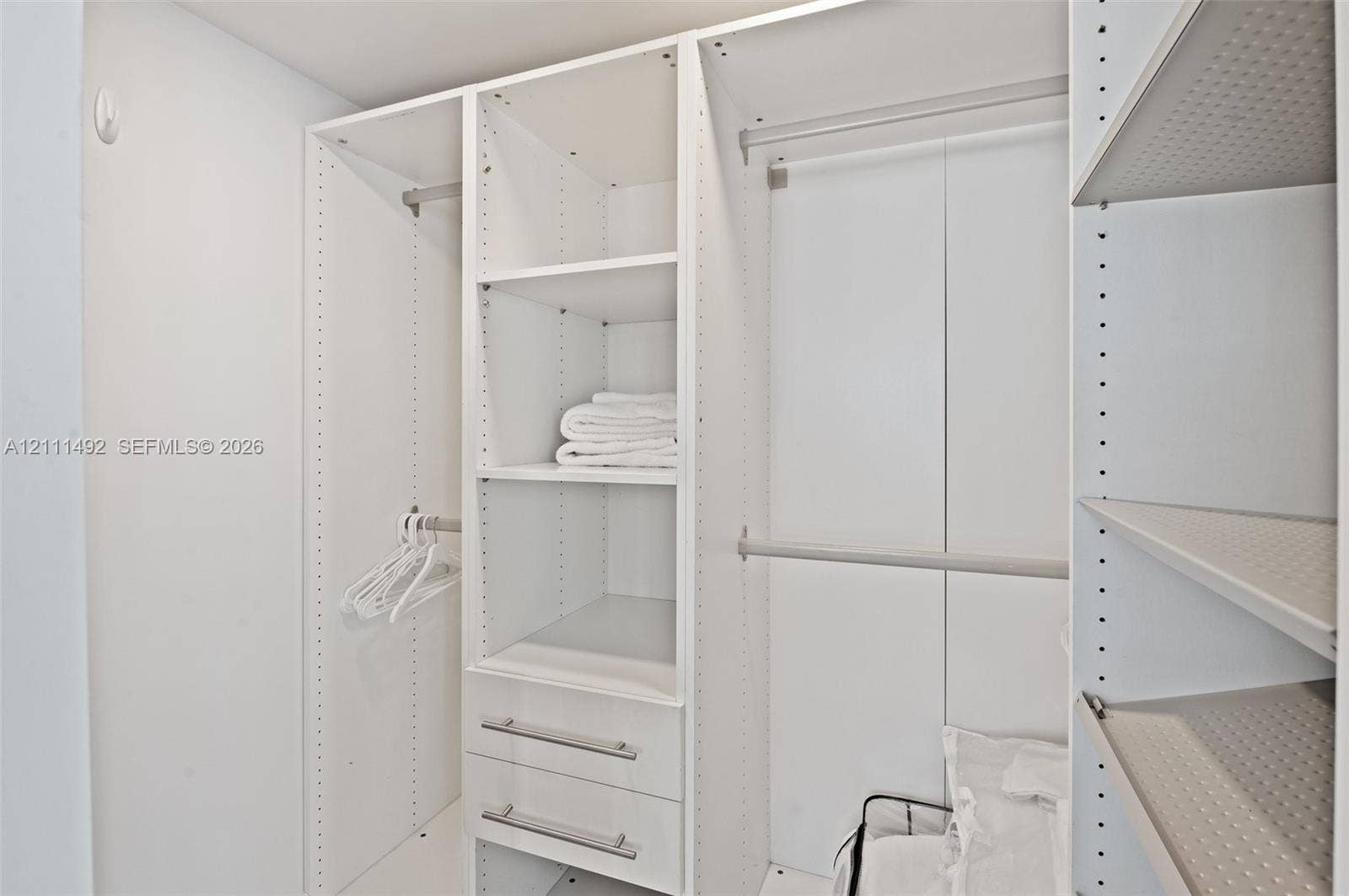 Custom walk-in closet featuring white modular built-in shelving, adjustable shelving units, integrated hanging rods, and two built-in storage drawers with metallic pulls