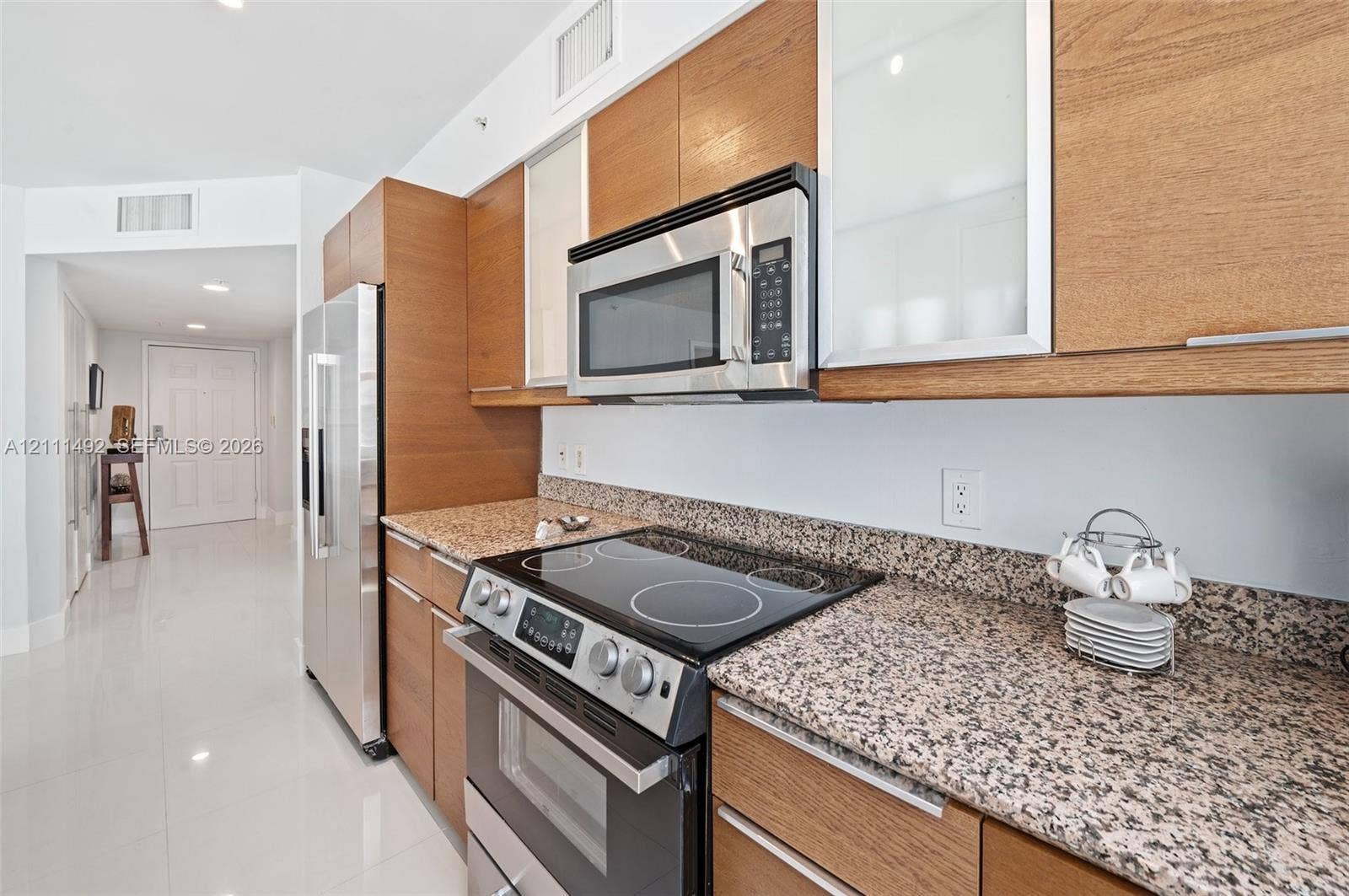 Kitchen featuring flat-panel wood cabinetry, speckled stone countertops, stainless steel appliances, and polished tile flooring
