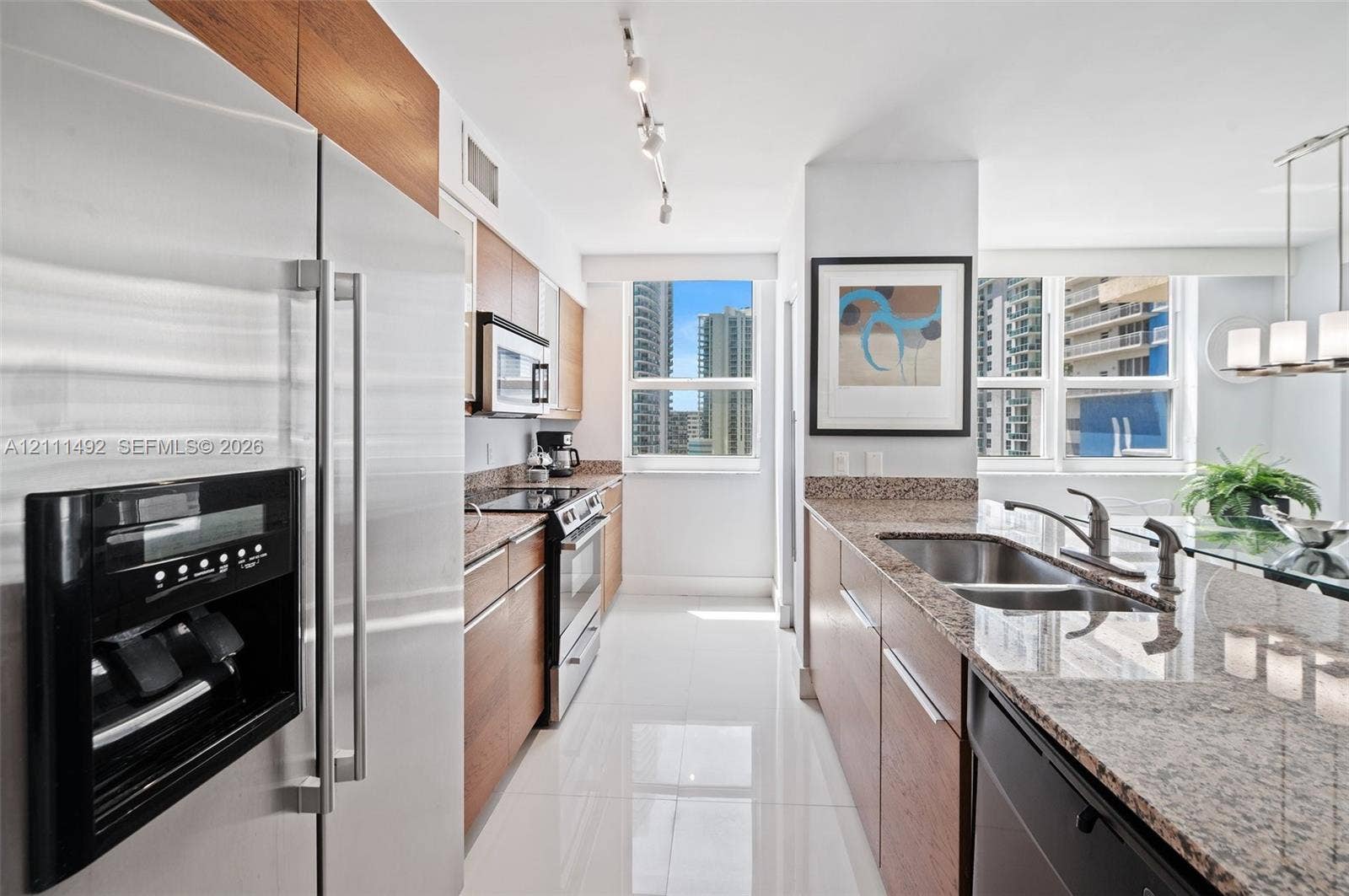Kitchen featuring wood-finish cabinetry, stone countertops, stainless steel appliances, a double-basin sink, and tile flooring