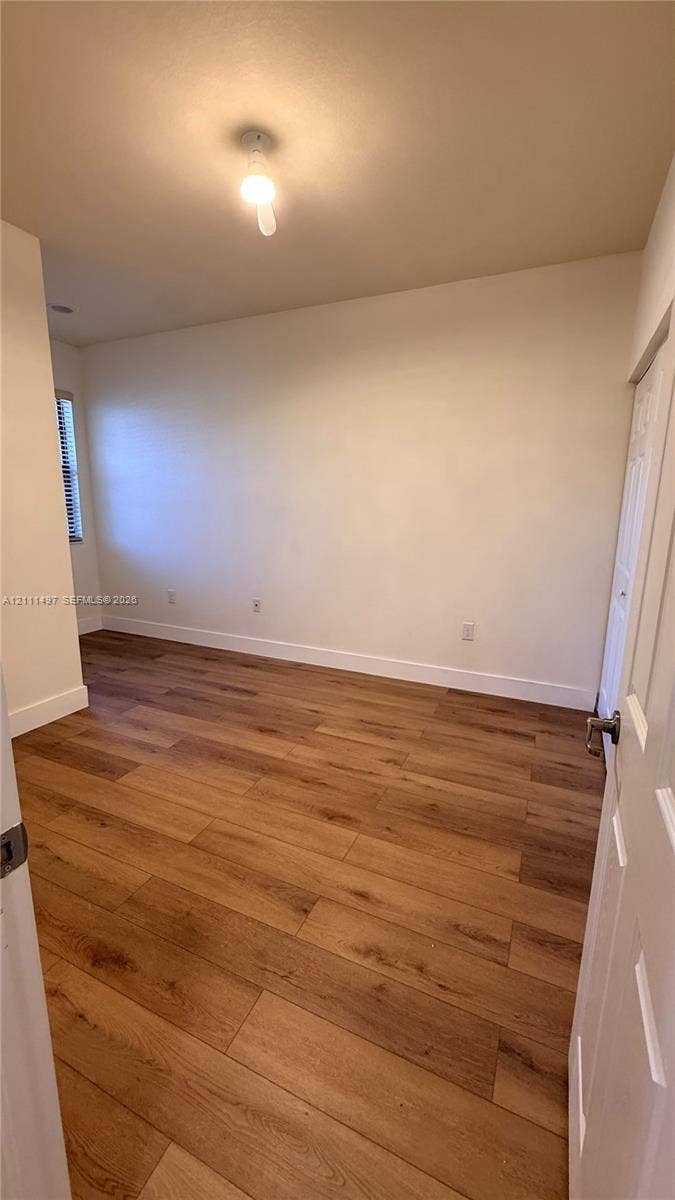 3210 SE 6th Street, Homestead, Homestead, FL 33033 Interior room featuring wood-finish flooring, neutral wall tones, a window with horizontal blinds, and a built-in closet