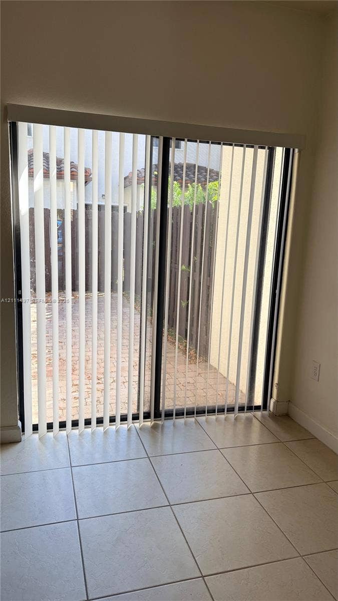 3210 SE 6th Street, Homestead, Homestead, FL 33033 Sliding glass door with vertical blinds, neutral tile flooring, and a paved outdoor patio area enclosed by a wooden fence
