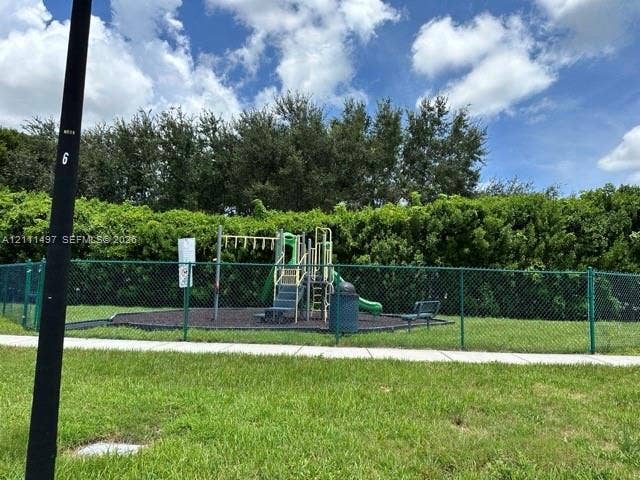 3210 SE 6th Street, Homestead, Homestead, FL 33033 Outdoor recreation area featuring a playground structure with a slide, chain-link perimeter fencing, and mature hedge landscaping