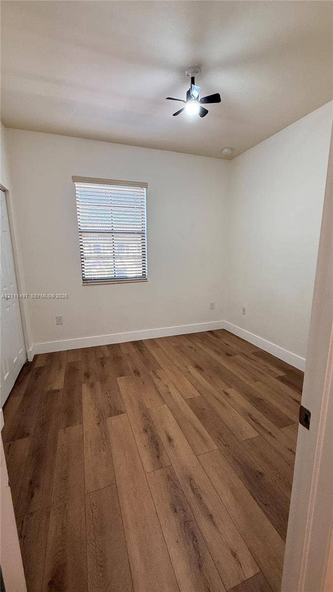 3210 SE 6th Street, Homestead, Homestead, FL 33033 Interior space featuring wood-finish flooring, a neutral wall palette, a single window with horizontal blinds, and a central ceiling fan with an integrated light fixture