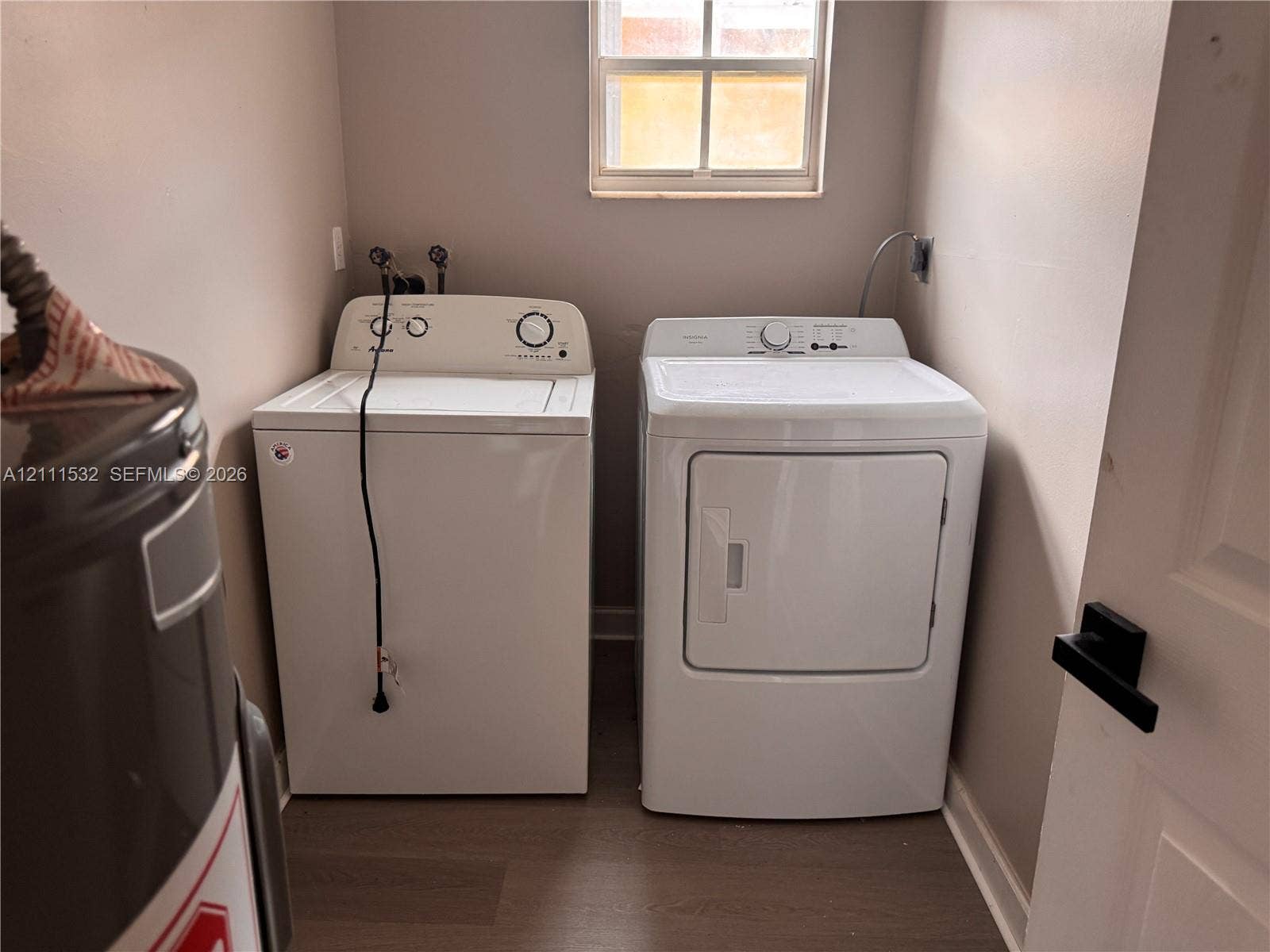 Dedicated laundry space featuring wood-finish flooring, a window, and a white interior door with matte black hardware