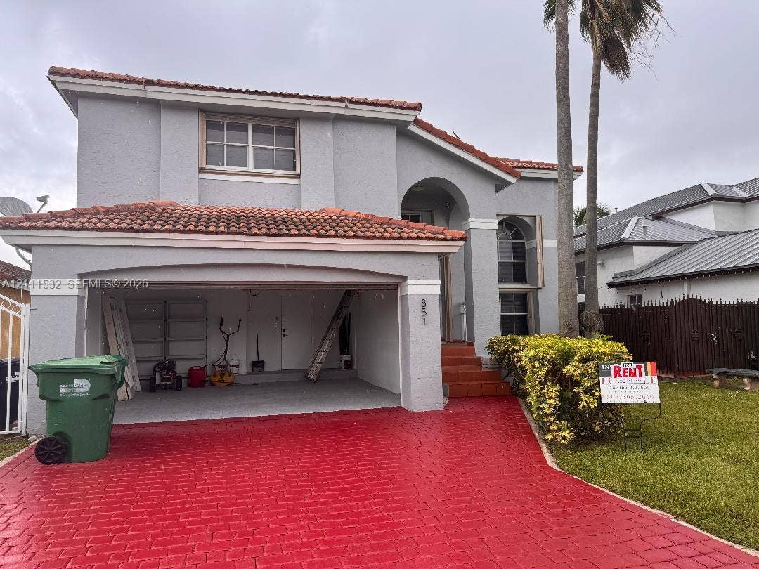 Two-story exterior featuring a stucco facade, red tile roofing, arched entryway, and patterned paver driveway