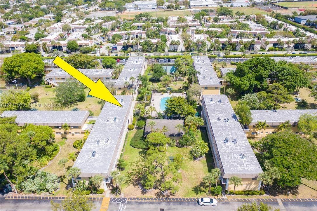 Aerial perspective of the residential complex featuring multi-story structures, integrated swimming pool, expansive landscaped grounds, and mature palm trees