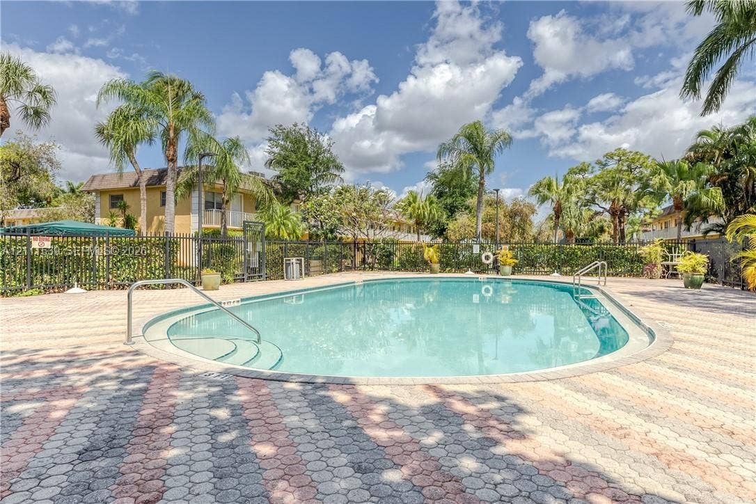 In-ground swimming pool with integrated stair entry, surrounded by patterned stone paver decking and enclosed by black metal perimeter fencing