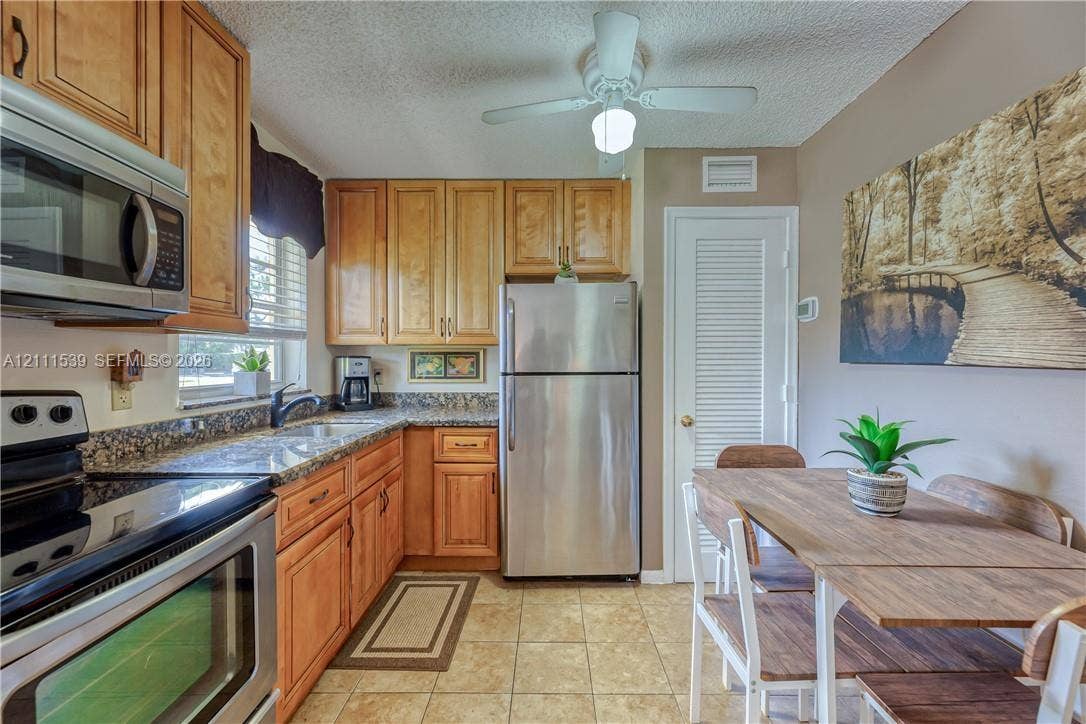 Kitchen featuring shaker-style cabinetry, stone countertops, stainless steel appliances, tile flooring, and a ceiling-mounted light fixture