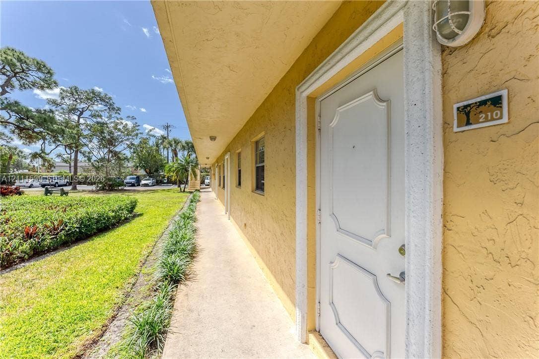 Stucco exterior featuring a covered concrete walkway, decorative panel door, and wall-mounted exterior lighting