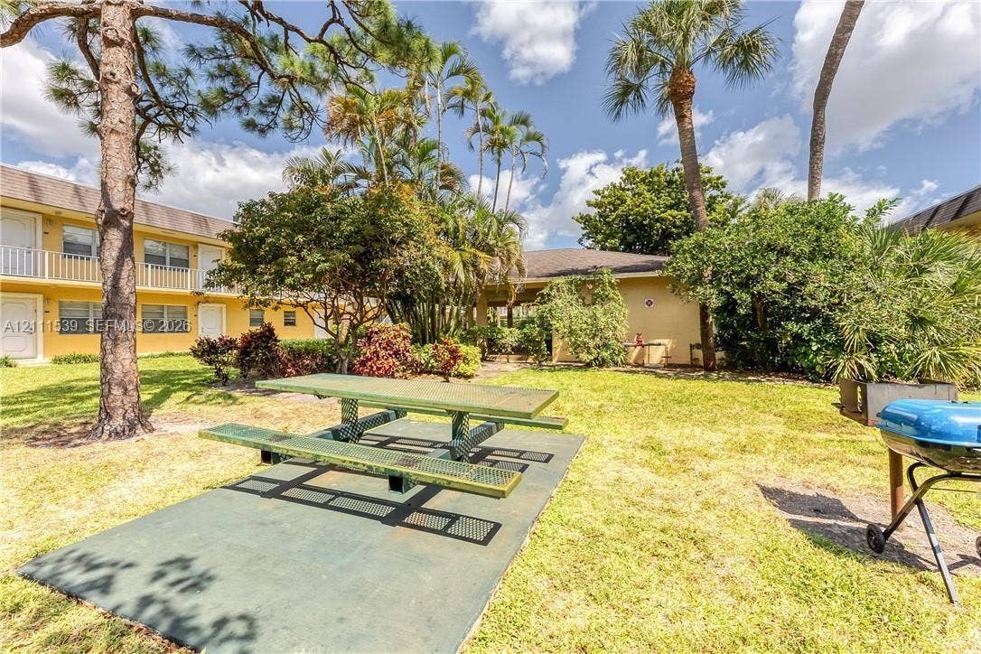 Common grounds featuring a grass lawn, mature palm trees, a paved seating area, and a metal picnic table