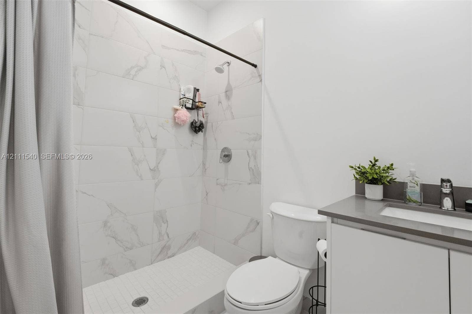 Shower enclosure featuring large-format veined tile surround, matte black shower hardware, and vanity with stone-finish countertop and integrated sink