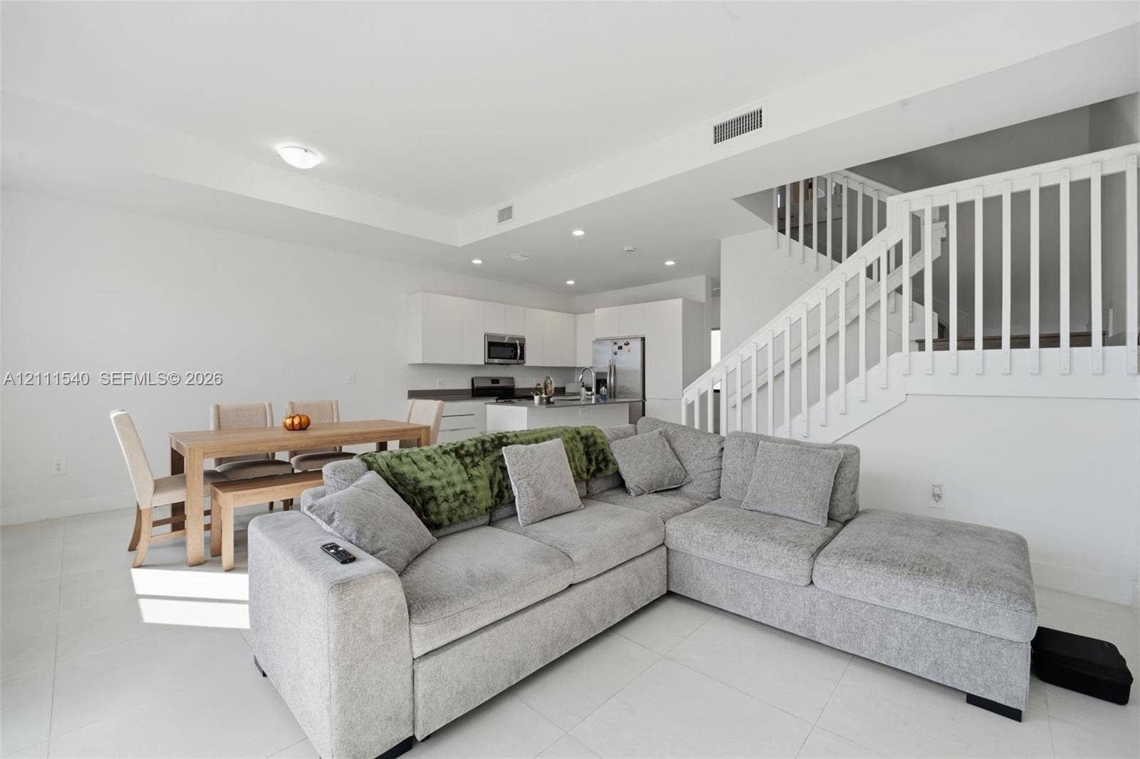 Open-concept living space featuring neutral tile flooring, recessed lighting, and a staircase with white vertical balusters