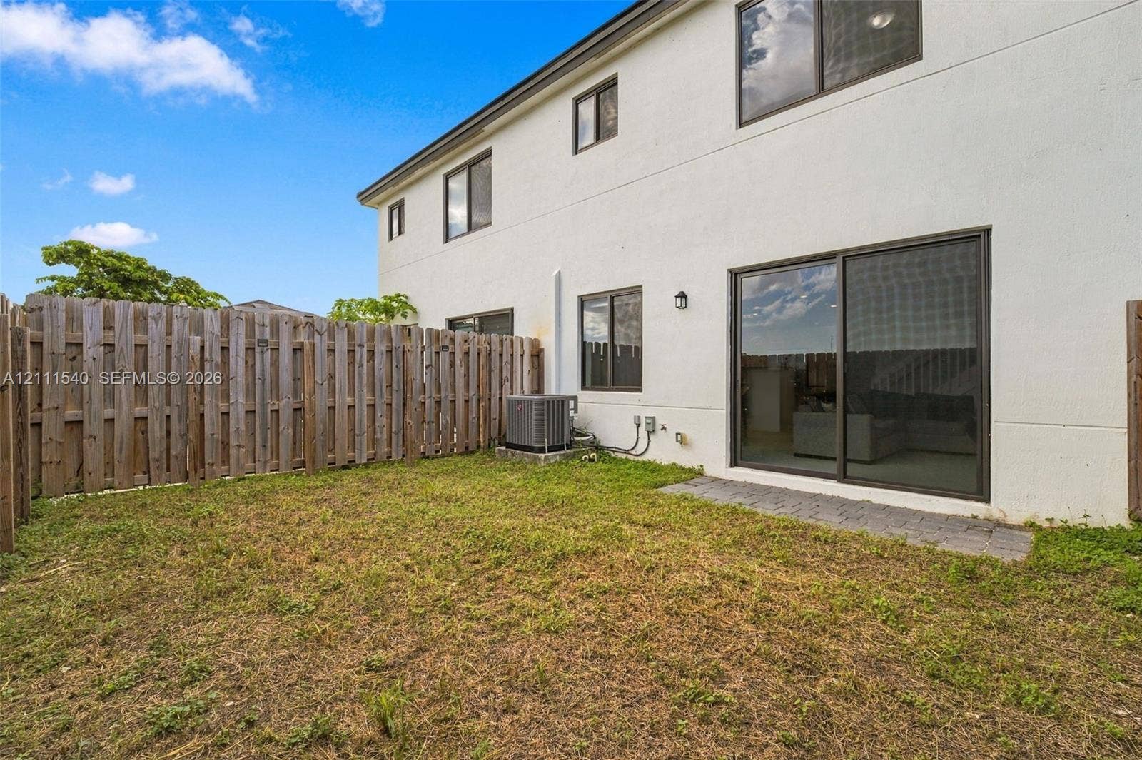 Rear exterior featuring a stucco facade, sliding glass patio door, paved stone patio, and wood privacy fencing
