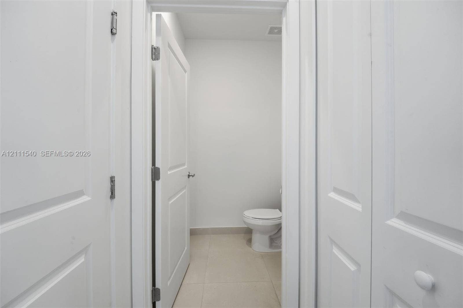 Neutral interior featuring white two-panel doors, neutral large-format floor tile, and a porcelain toilet