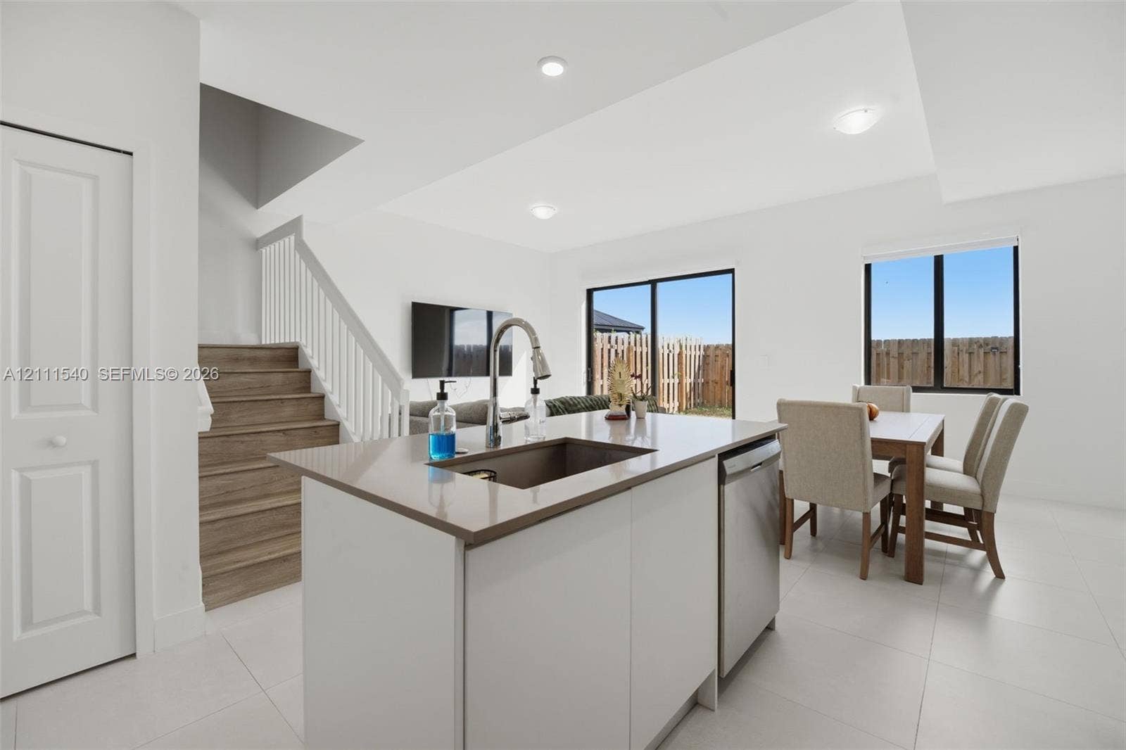 Kitchen island with stone-surface countertop, stainless steel undermount sink, wood-finish stairs with white railing, and sliding glass doors