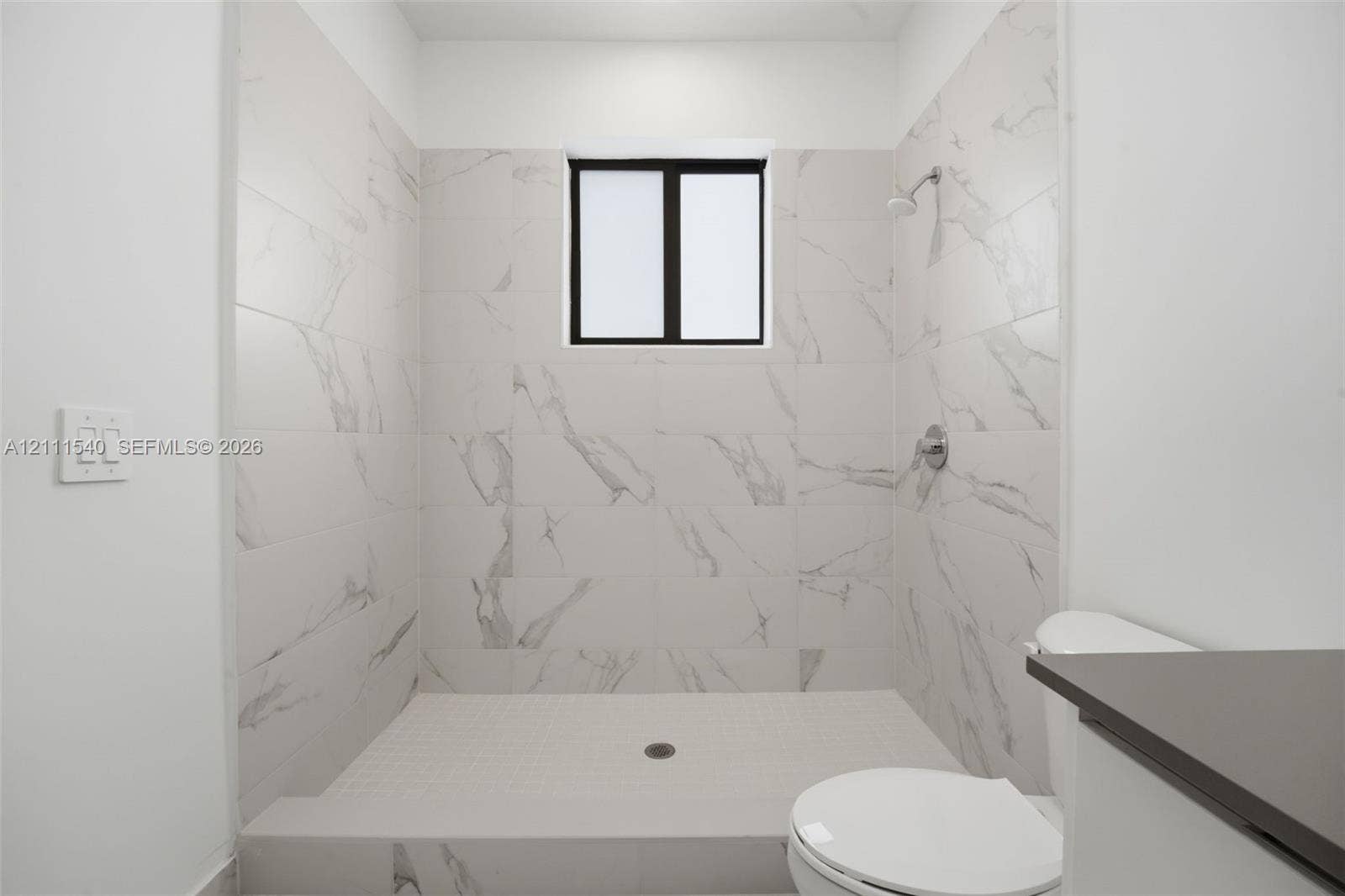 Walk-in shower featuring floor-to-ceiling stone-finish tile surround, a built-in shower head, and a privacy window