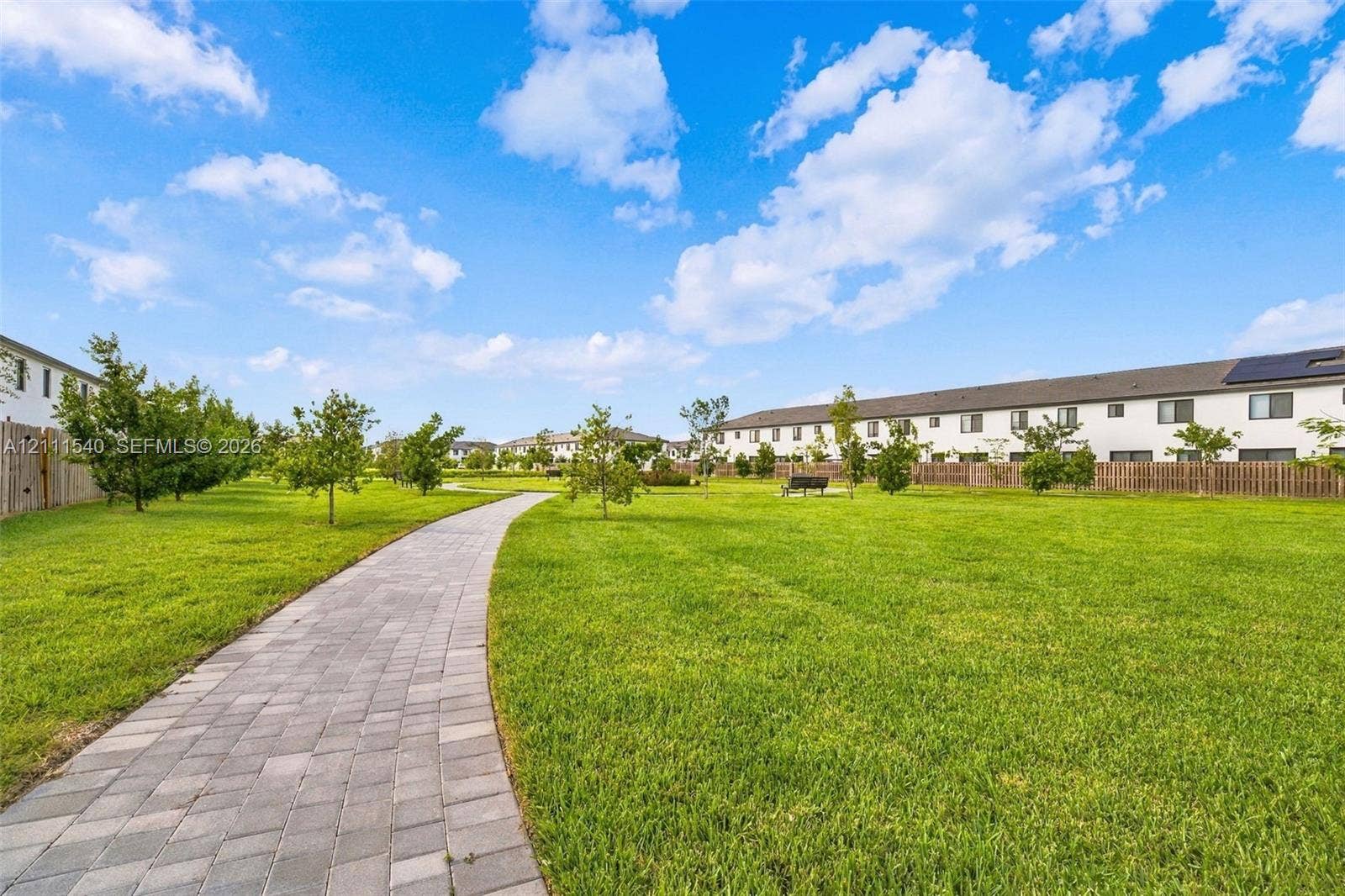 Expansive common area featuring a manicured lawn, paver stone walkway, and mature landscaping