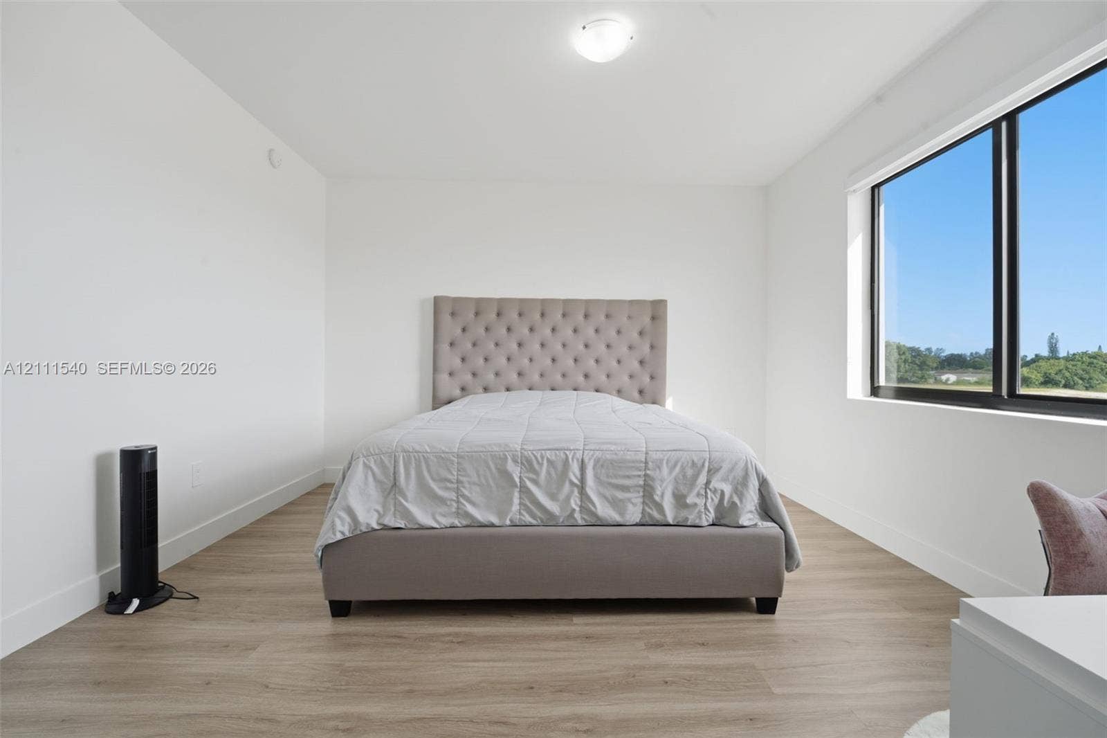 Minimalist room featuring white walls, wood-finish flooring, and a large window