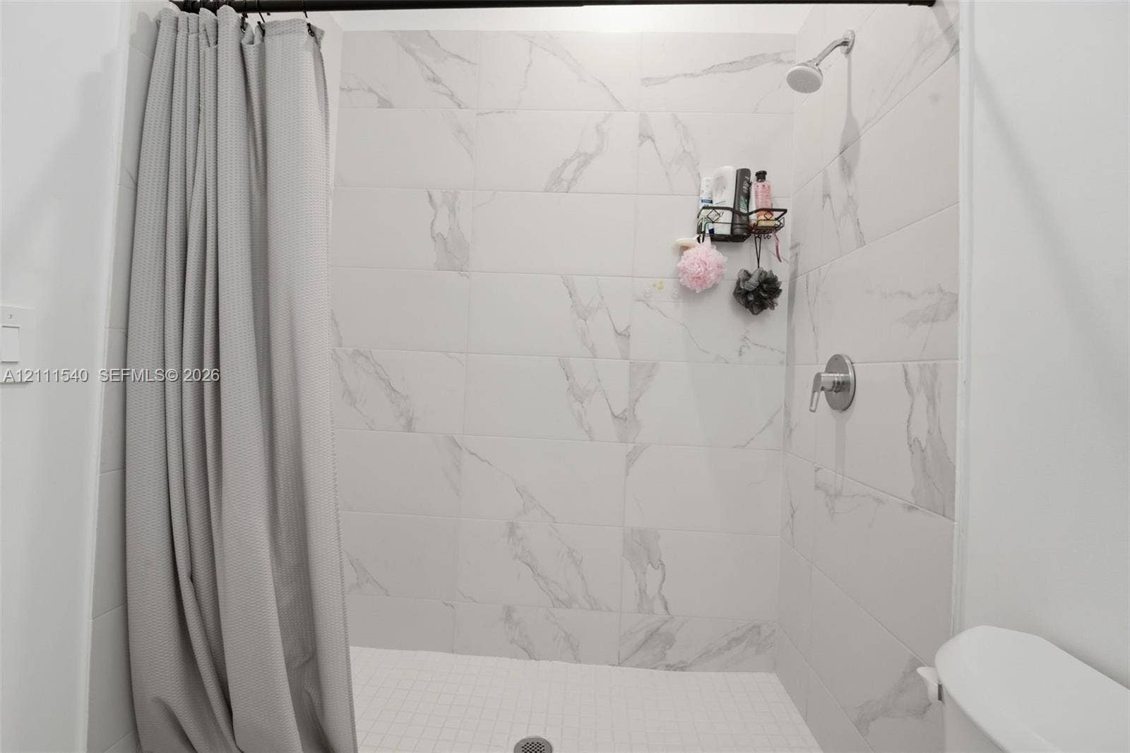 Shower enclosure featuring large-format light-toned stone-finish wall tile with prominent veining, a wall-mounted showerhead, and a single-handle pressure balance valve