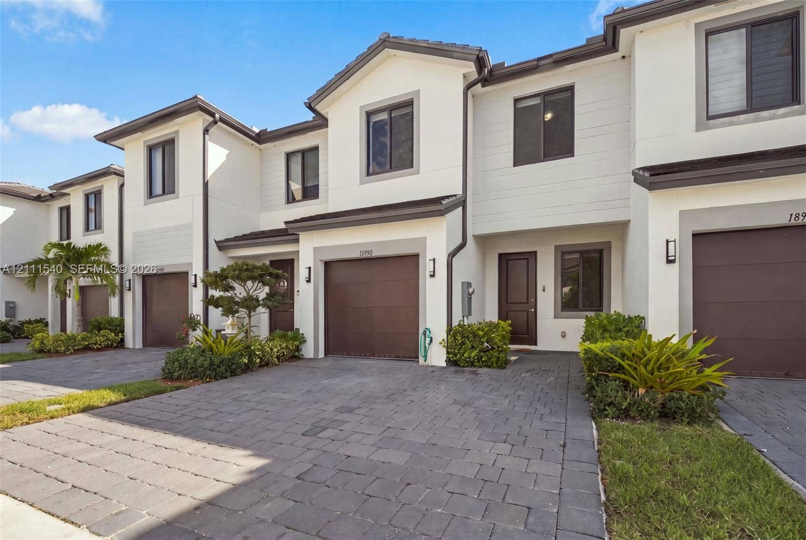 Multi-level townhouse exterior featuring a paver driveway, an attached garage, and a light-toned stucco faade