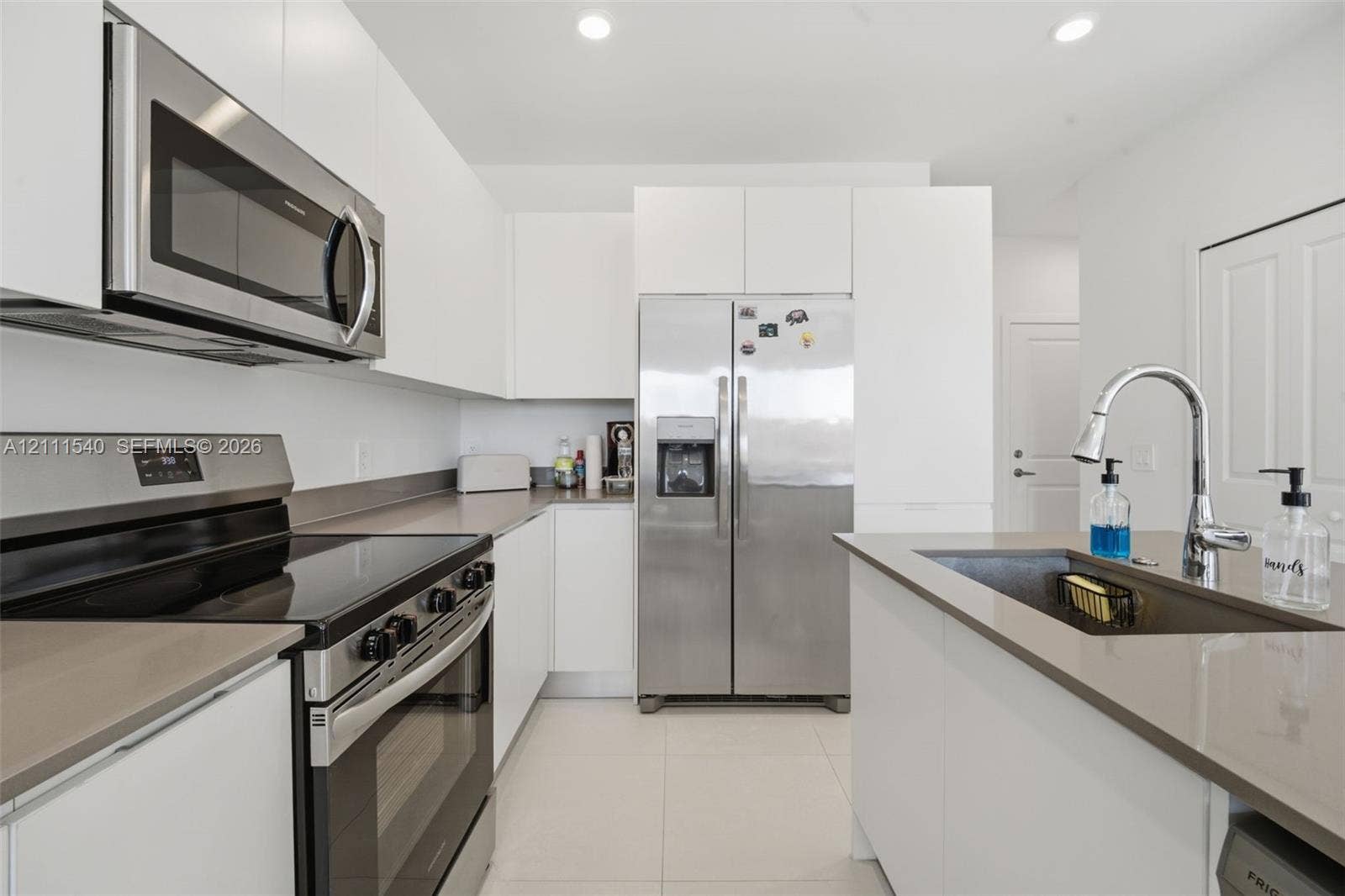 Kitchen featuring flat-panel white cabinetry, stainless steel appliances, quartz countertops, an undermount sink with a gooseneck faucet, and tile flooring