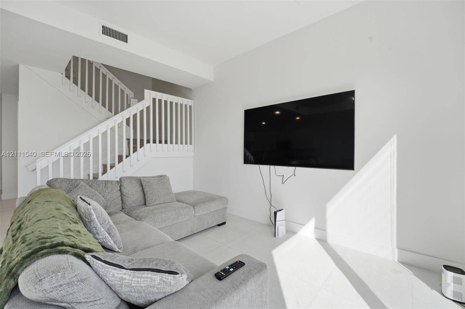 Neutral interior featuring large-format tile flooring, crisp white walls, and a staircase with white vertical balusters