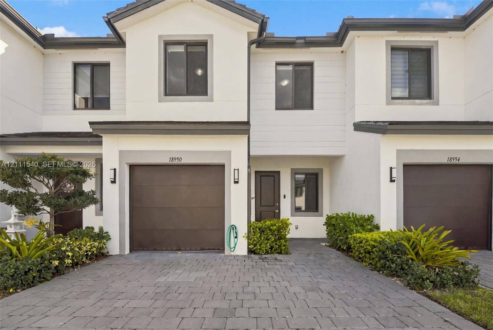 Two-story exterior featuring white stucco siding, gray trim, paved driveway, single-car garage, and manicured landscaping