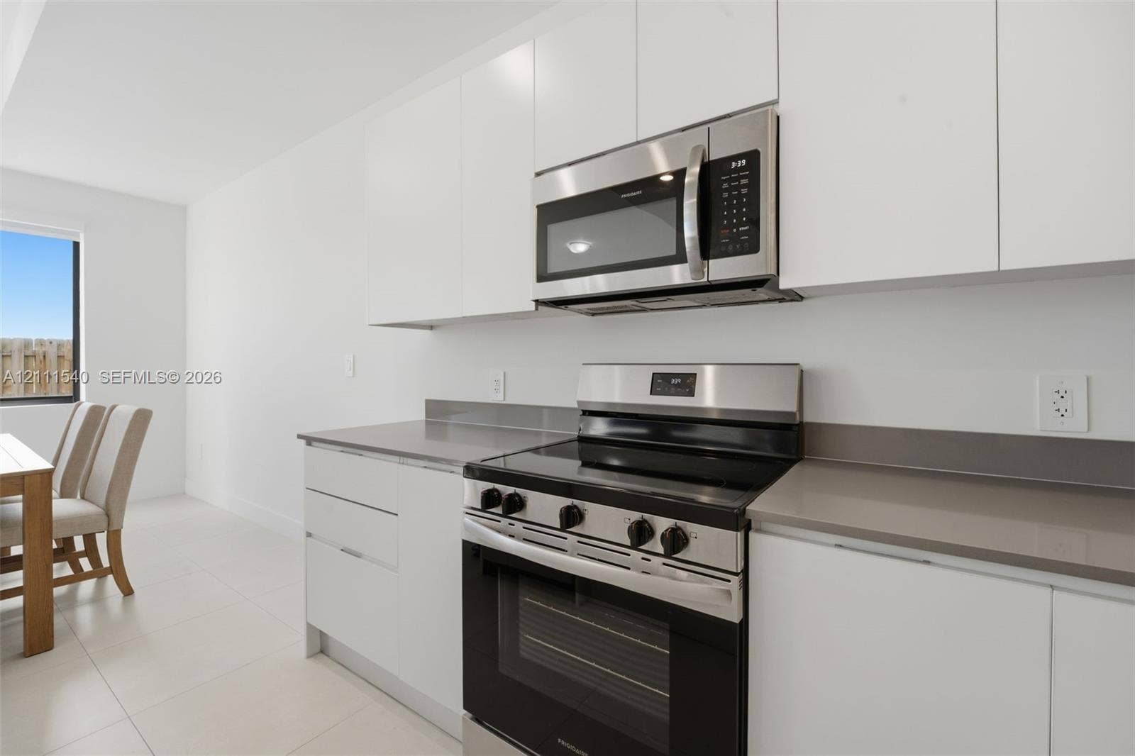 Kitchen featuring flat-panel white cabinetry, solid-surface countertops, and stainless steel appliances including an over-the-range microwave and electric range