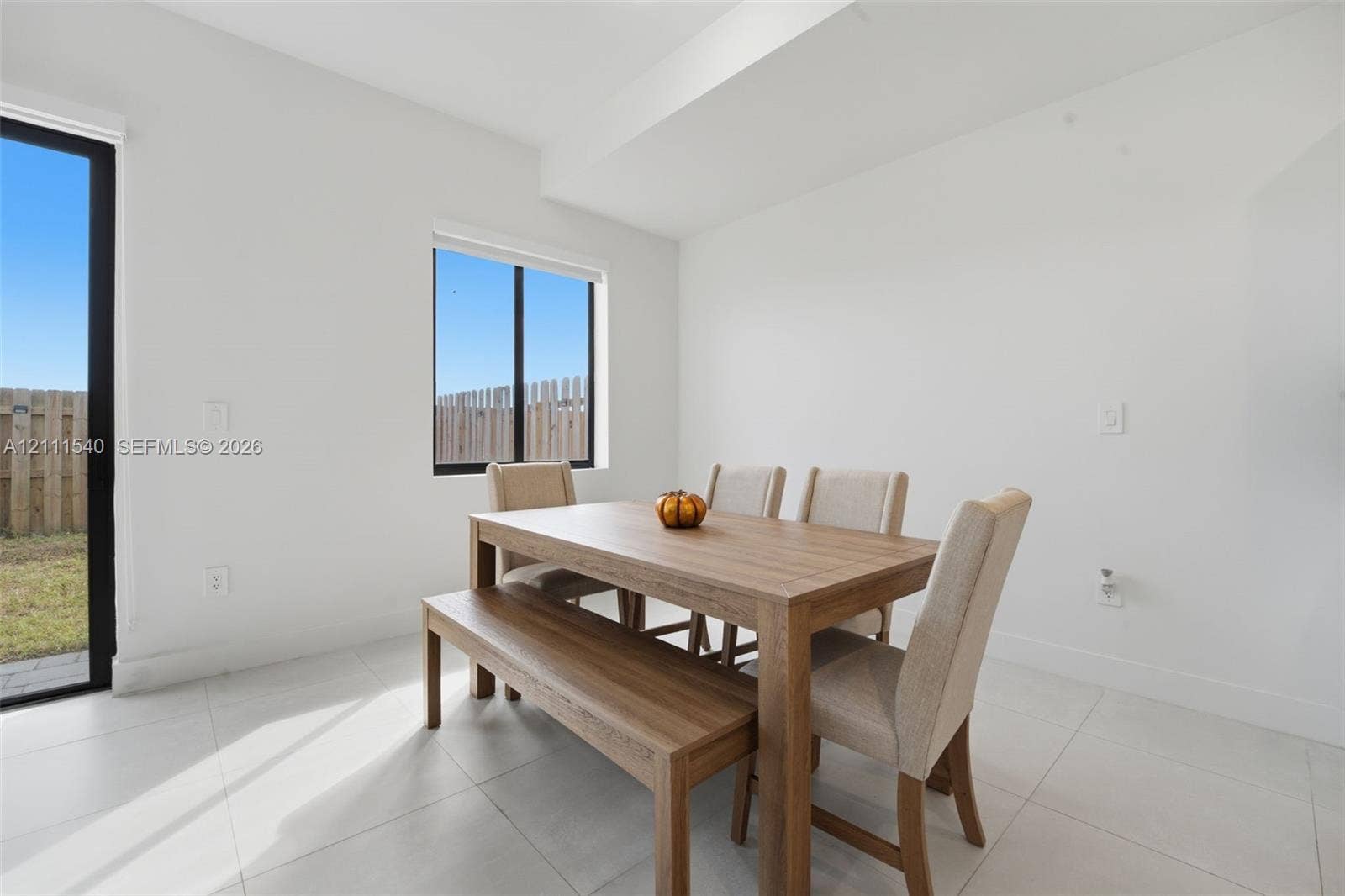 Neutral-toned tile flooring, minimalist white walls, and a large sliding glass door featuring a black frame