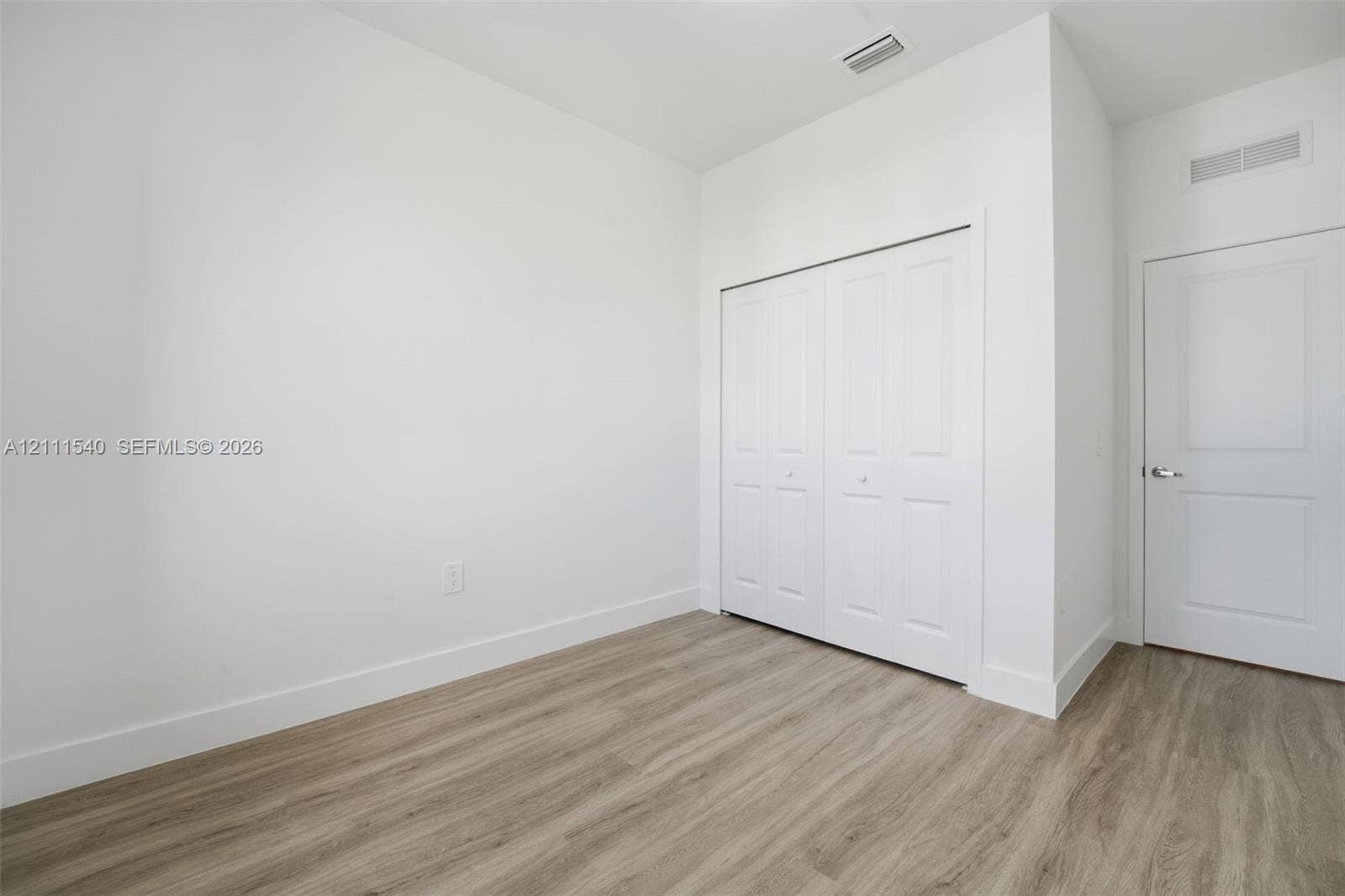 Neutral-toned room featuring wood-finish flooring, a double-panel closet, and a white interior door with metallic hardware