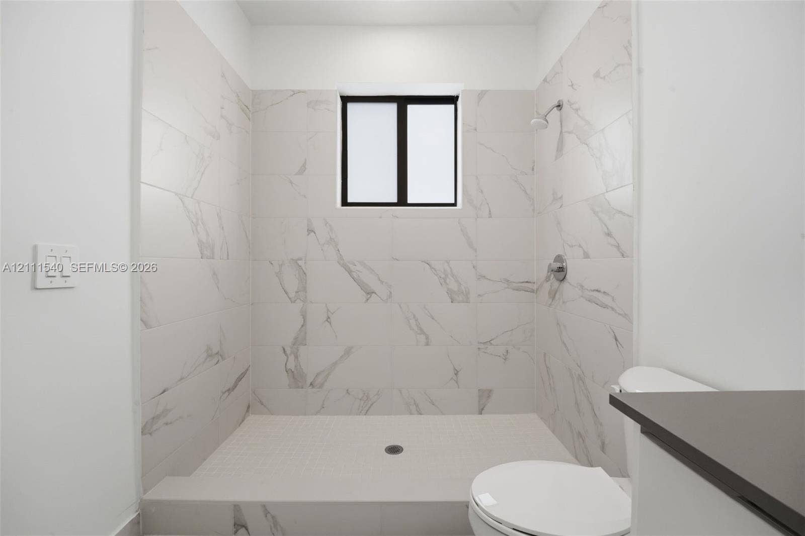 Walk-in shower enclosure featuring large-format stone-patterned tile walls, fixed window, chrome shower fixture, and built-in shower floor