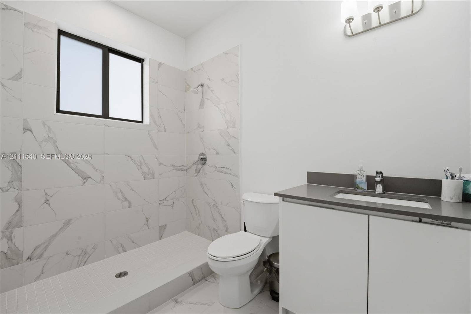 Bathroom featuring a walk-in shower with large-format stone-patterned tile, a vanity with a solid-surface countertop and integrated sink, and wall-mounted vanity lighting
