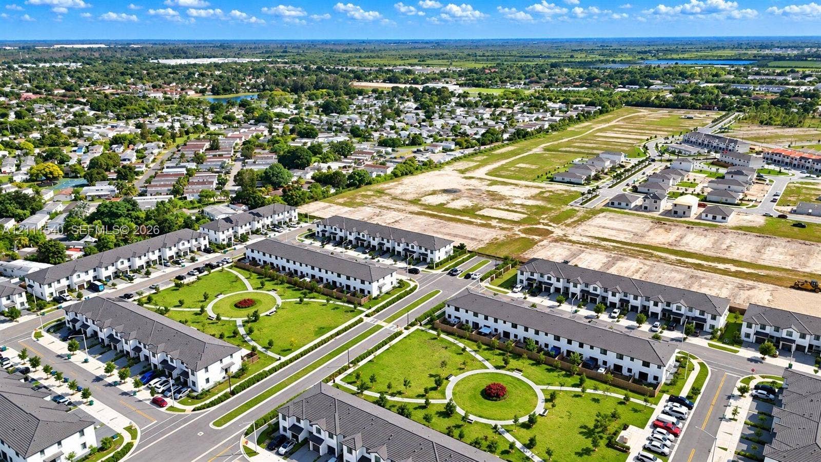Aerial perspective of a multi-unit residential community featuring manicured common green spaces, paved roadways, and planned development infrastructure