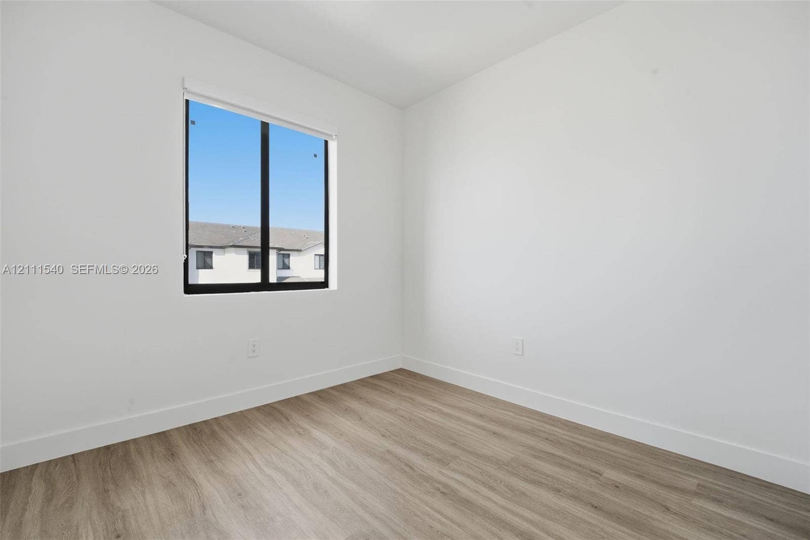 Neutral-toned interior space featuring wood-finish flooring, crisp white walls, and a large window with a black frame