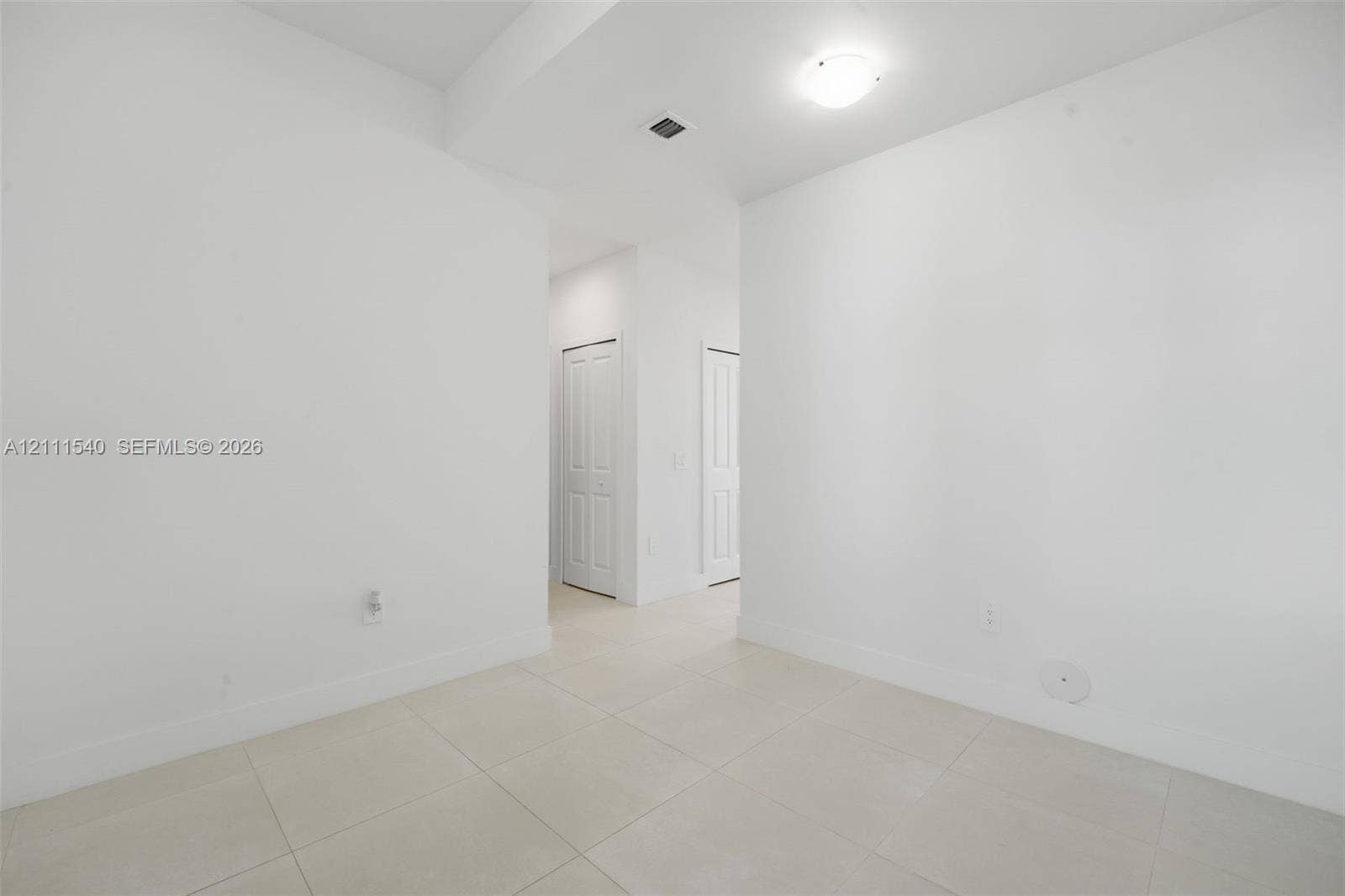 Neutral interior space featuring large-format ceramic tile flooring, crisp white walls, and two multi-panel interior doors